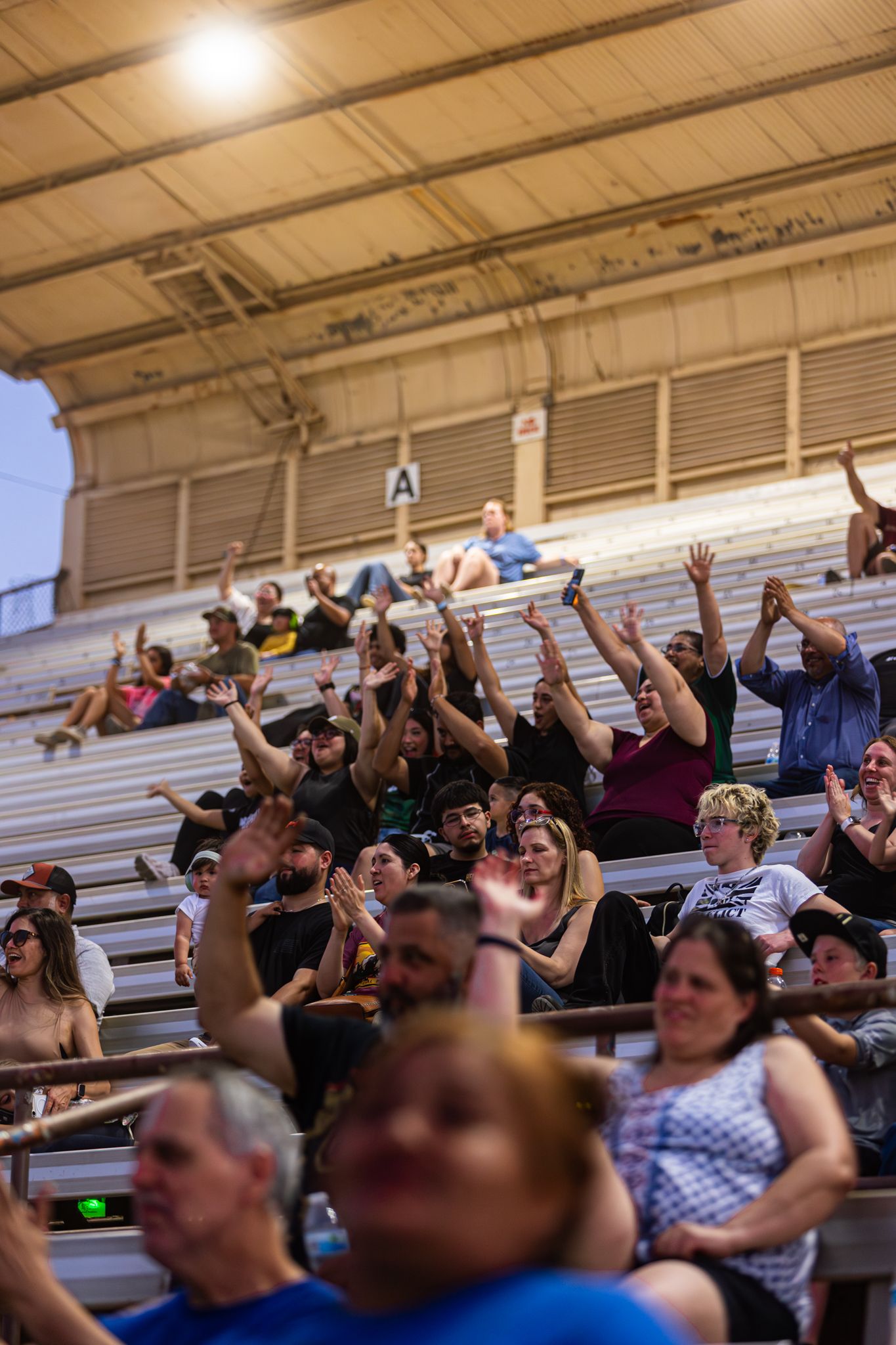 Excited crowd cheering with hands raised in bleachers at an outdoor stadium event under bright lights.