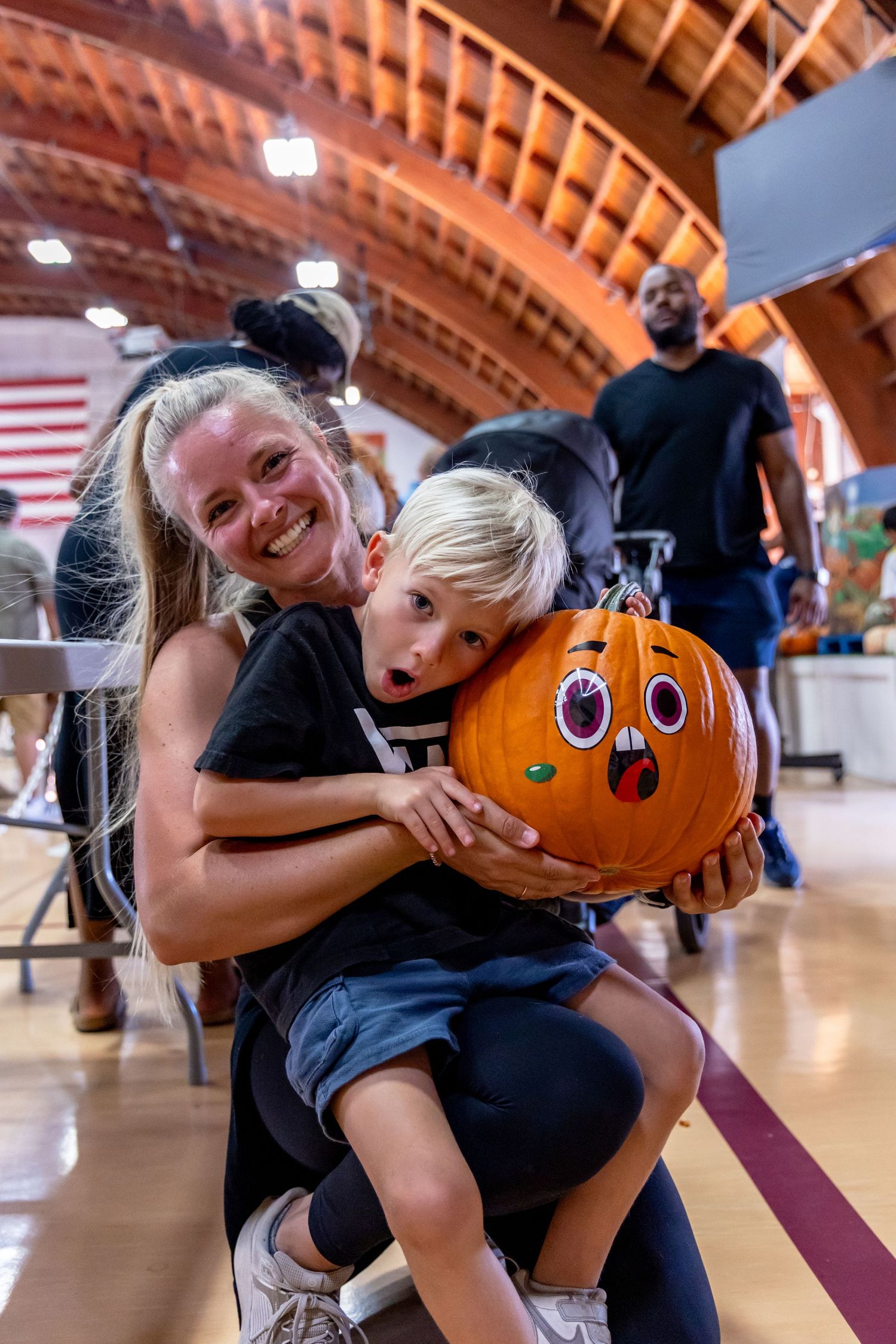 Smiling woman hugs a child holding a decorated Halloween pumpkin indoors.