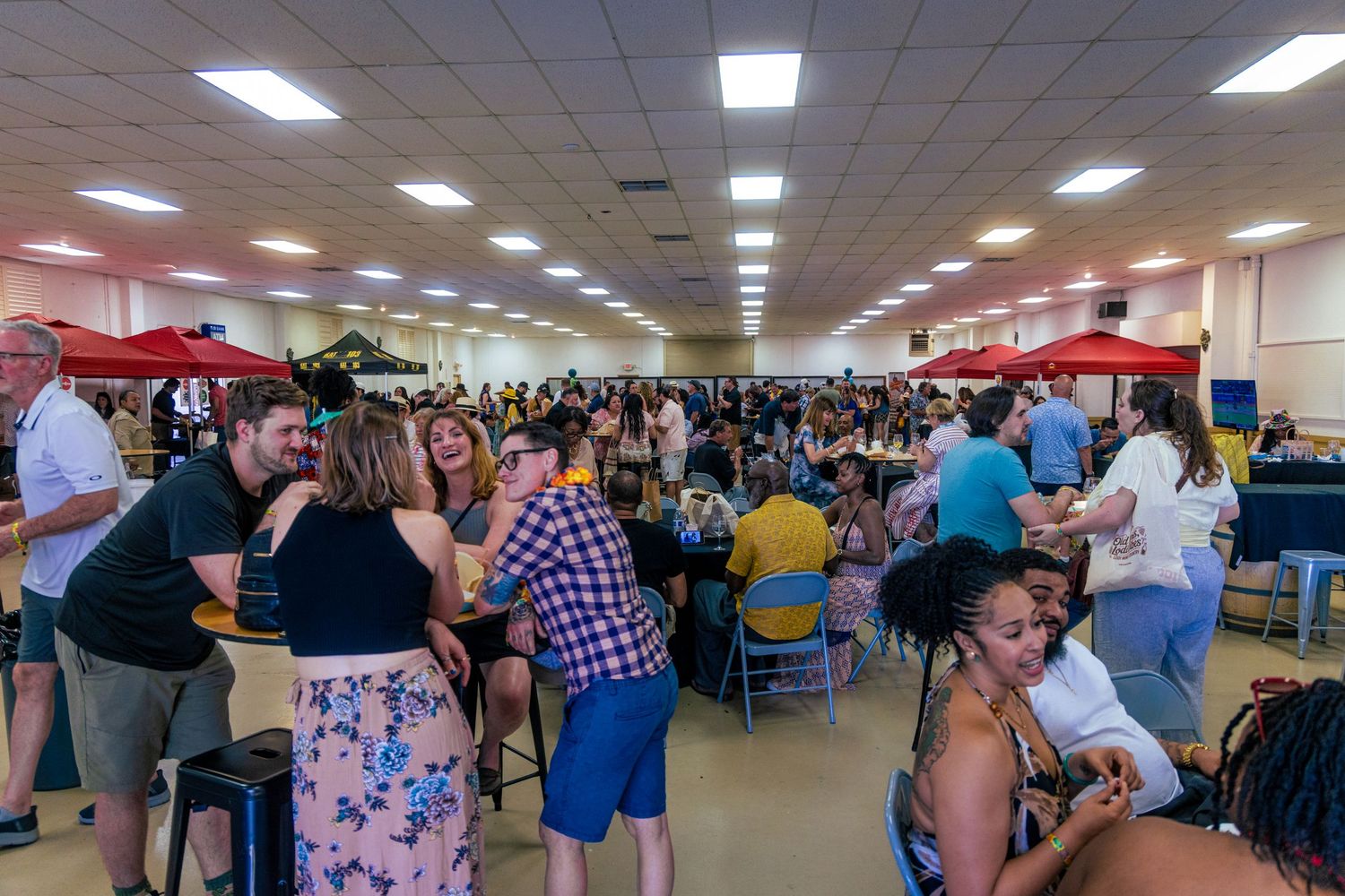 A large indoor food and drink festival with crowds of people socializing at tables under bright lights.