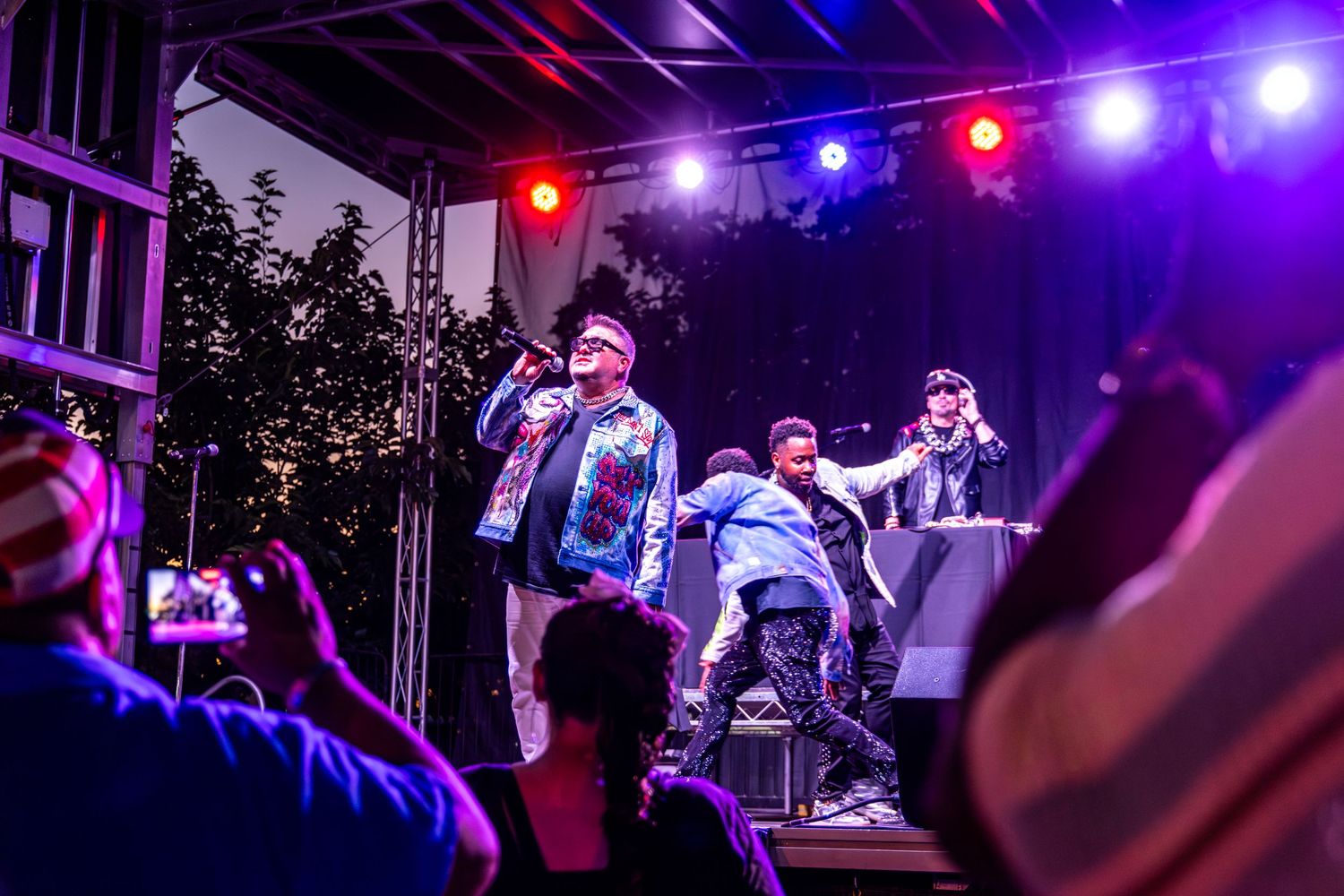 Hip-hop performers energize a crowd on a colorful lit outdoor stage at a live music concert event.