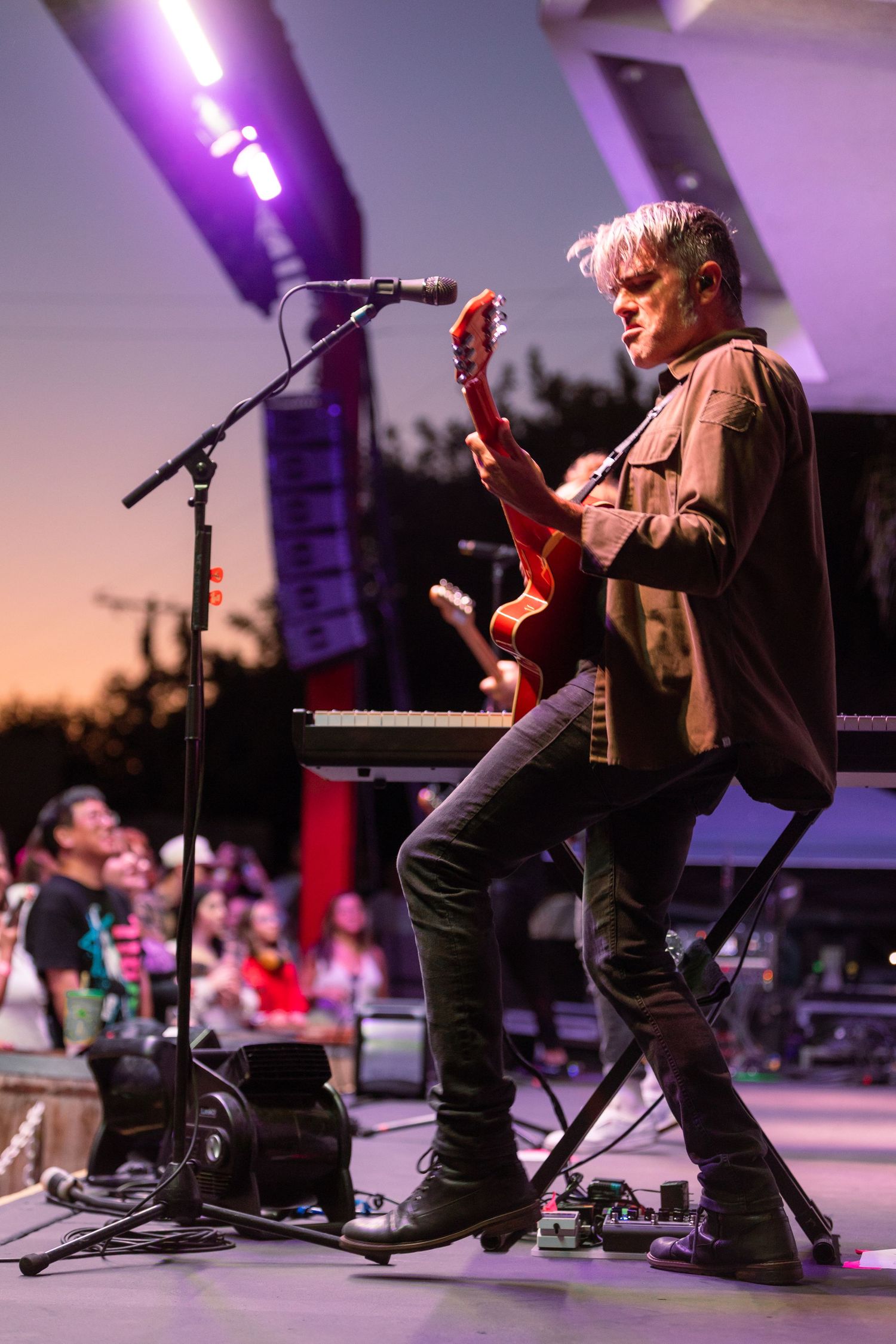 Male guitarist performs on stage at sunset during an outdoor music festival.