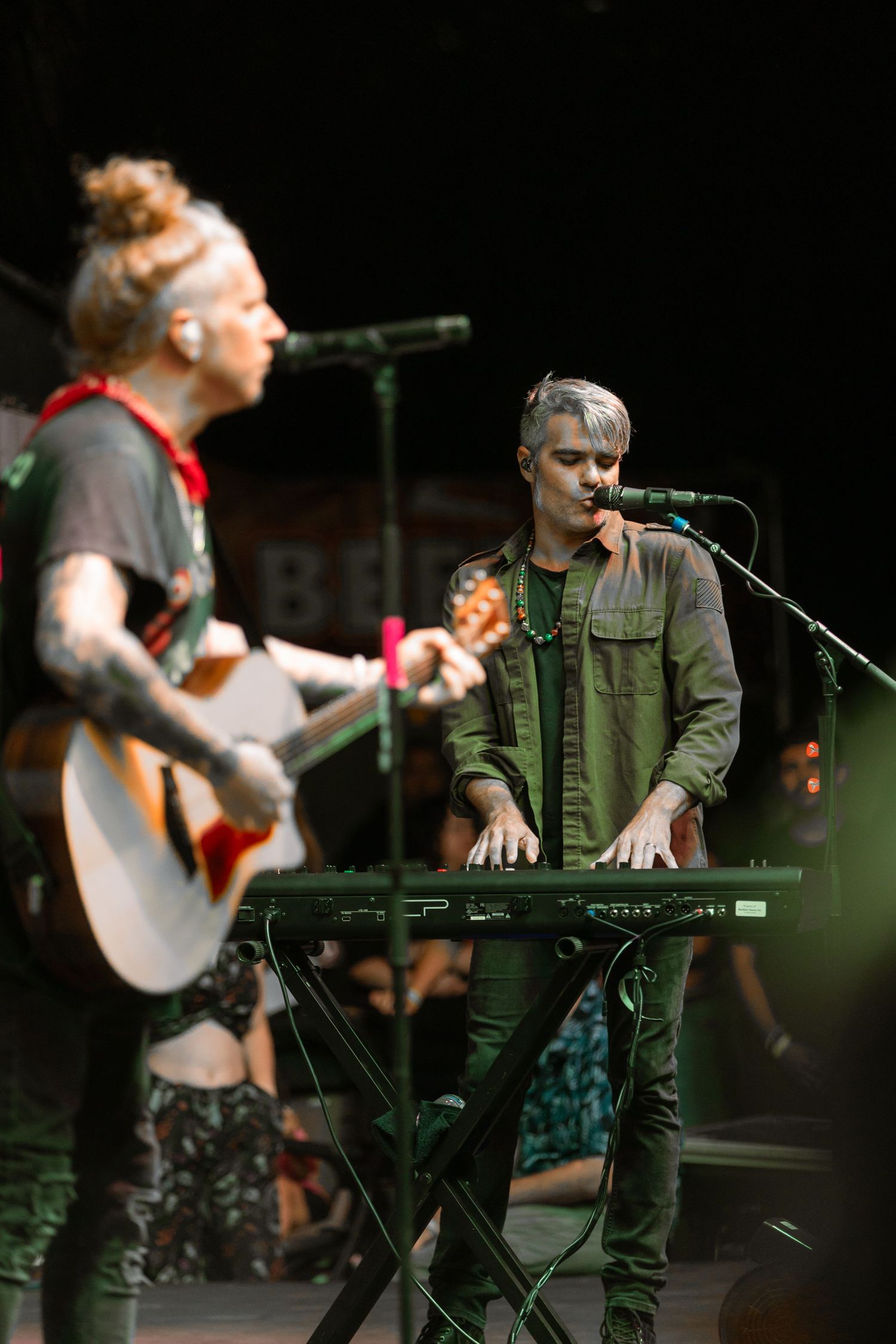 Two musicians perform on stage, one playing acoustic guitar and another on keyboard at a live concert.
