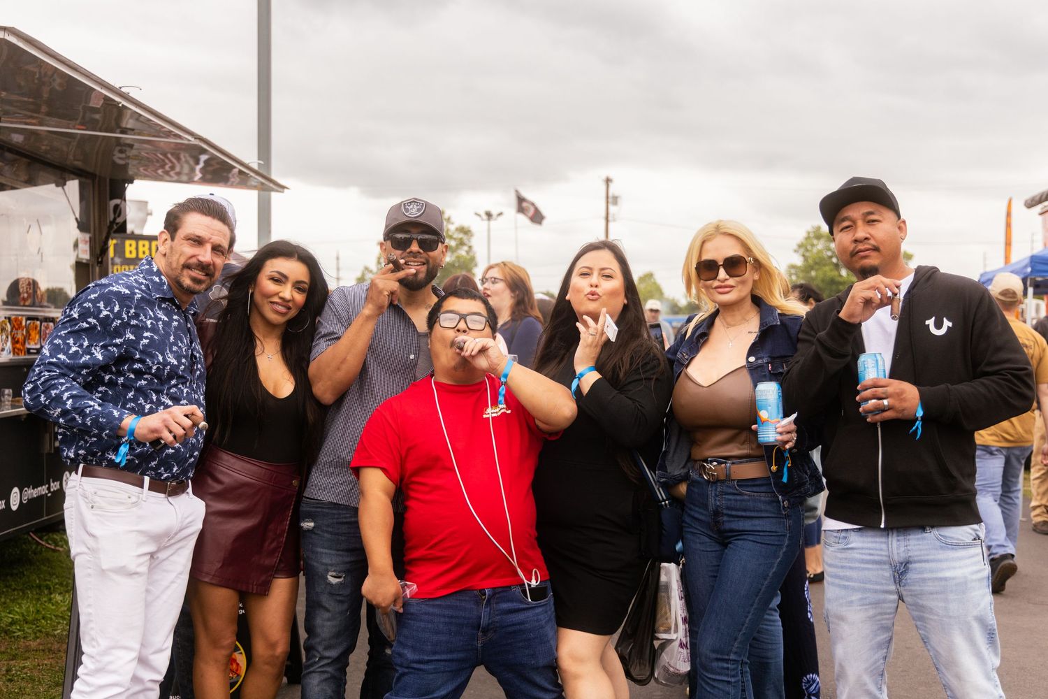 Group of friends posing and smiling together at an outdoor festival event on a cloudy day.