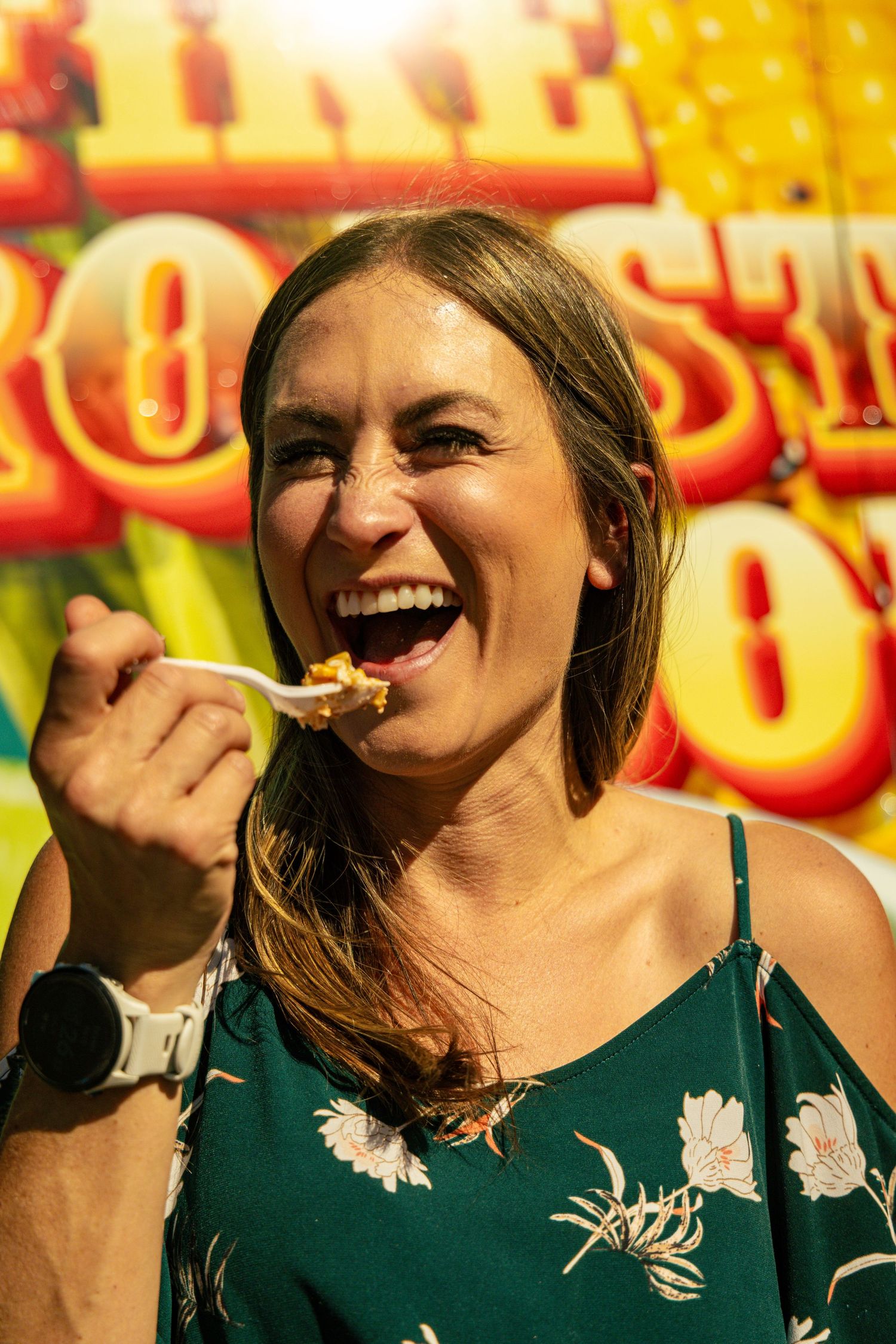 Happy woman eating food on a spork at a sunny outdoor carnival.