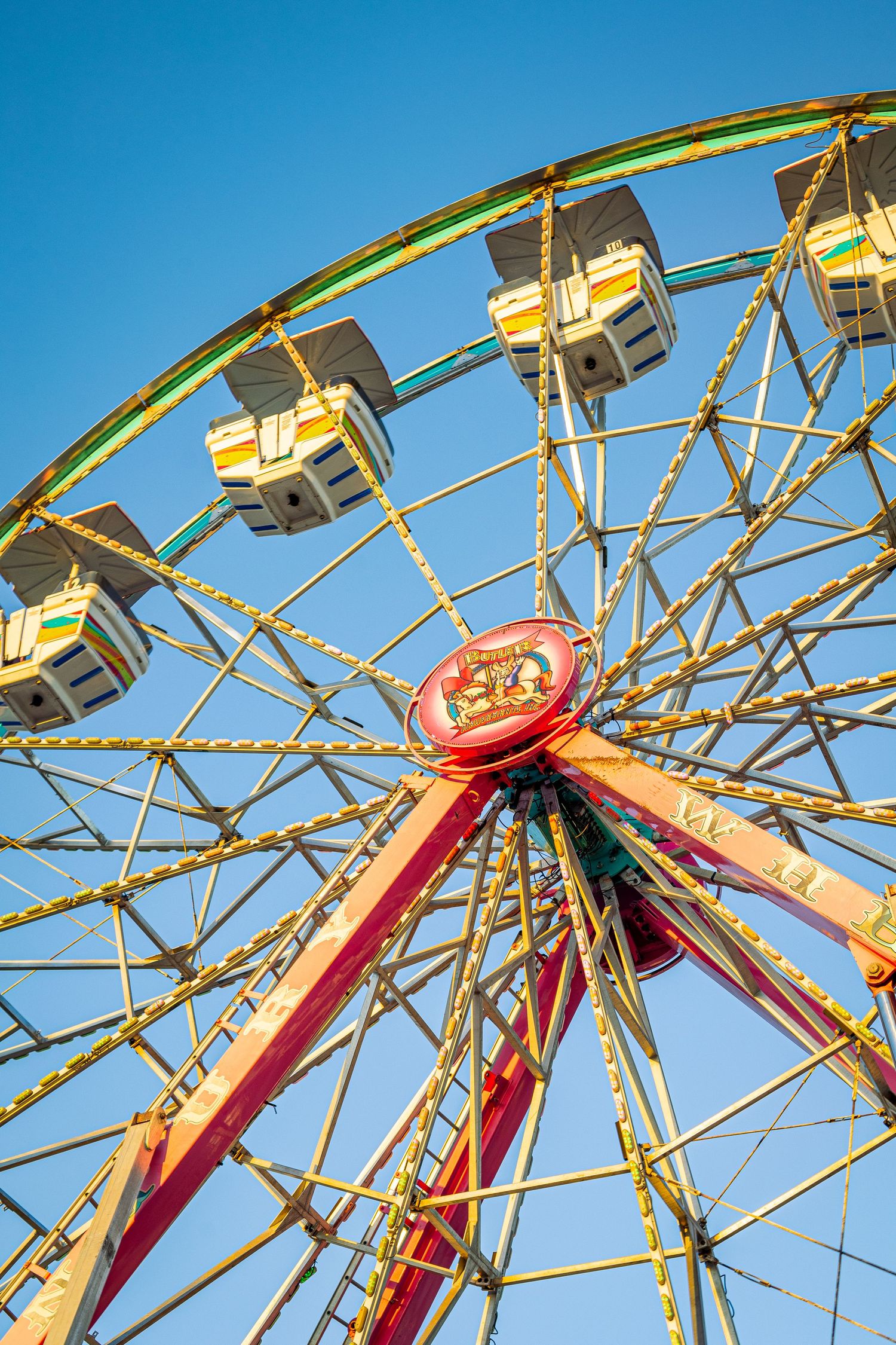 Colorful ferris wheel with white gondolas against a clear blue sky at an amusement park or county fair.