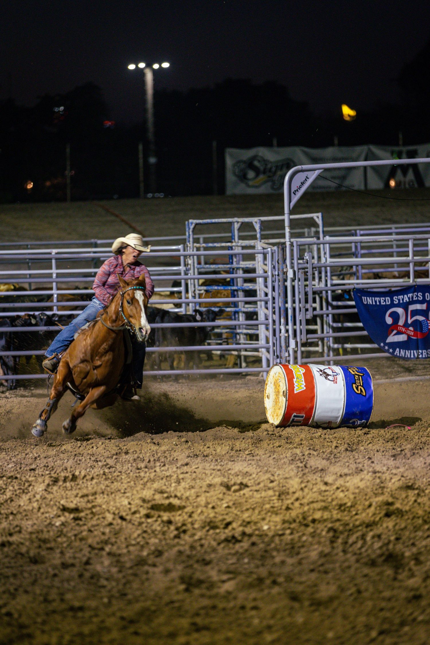 Cowgirl on horseback competes in barrel racing at a nighttime rodeo event.