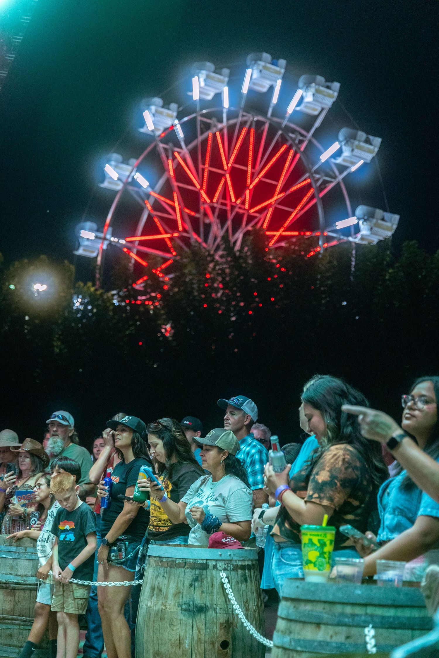 Crowd enjoying a nighttime fair with a glowing red Ferris wheel in the background.