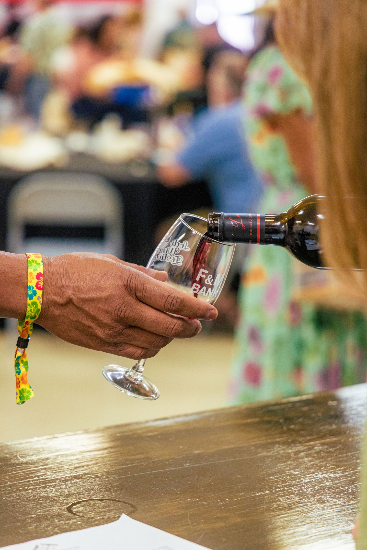 Close-up of wine being poured into a glass at a wine tasting event with colorful wristband.