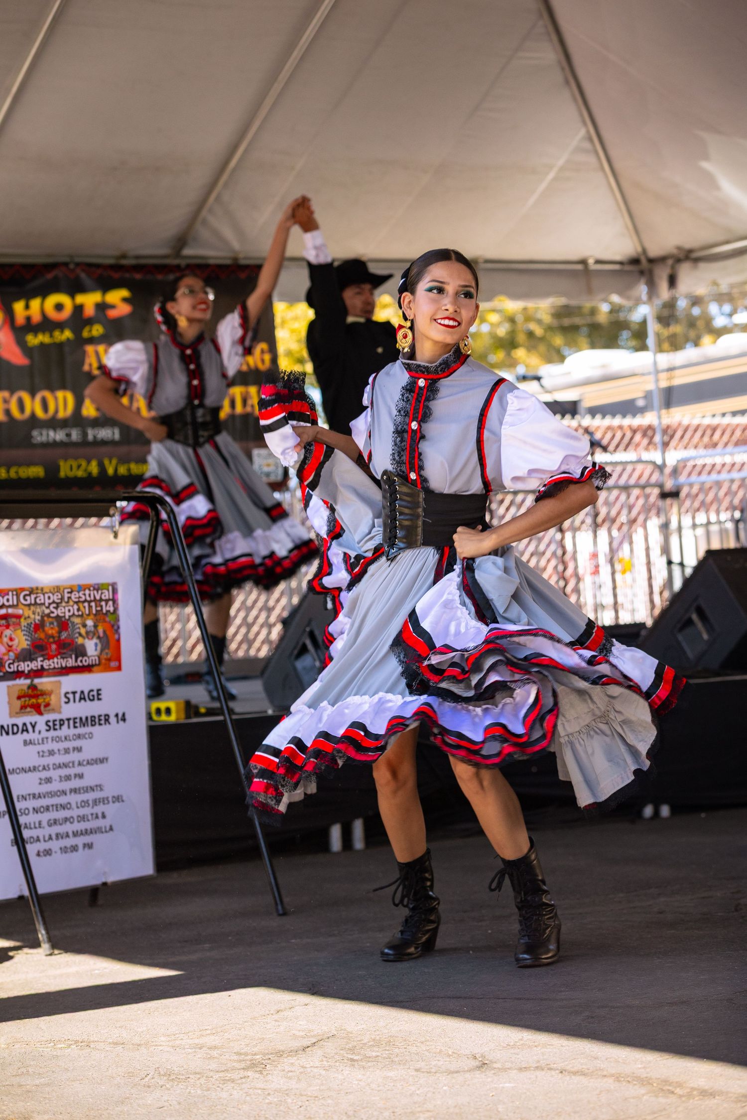 Female dancer in colorful traditional dress performs folkloric dance on an outdoor stage.