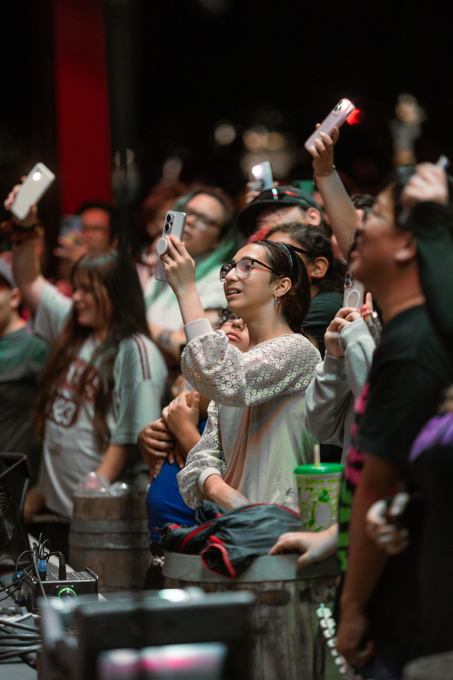 Smiling young woman holds up her phone to record a live concert surrounded by an enthusiastic crowd.