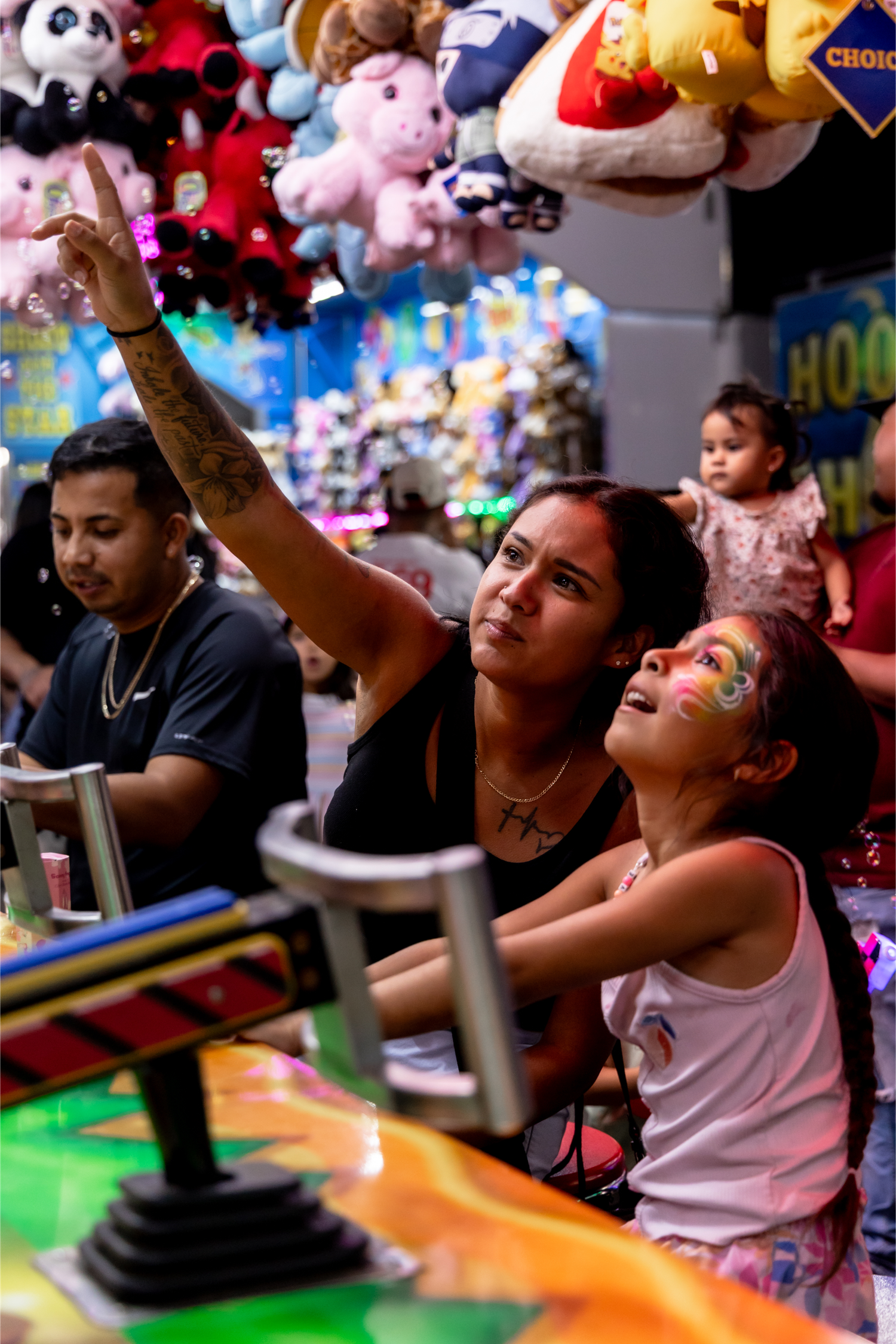 Woman and face-painted girl play an arcade game surrounded by stuffed animal prizes.