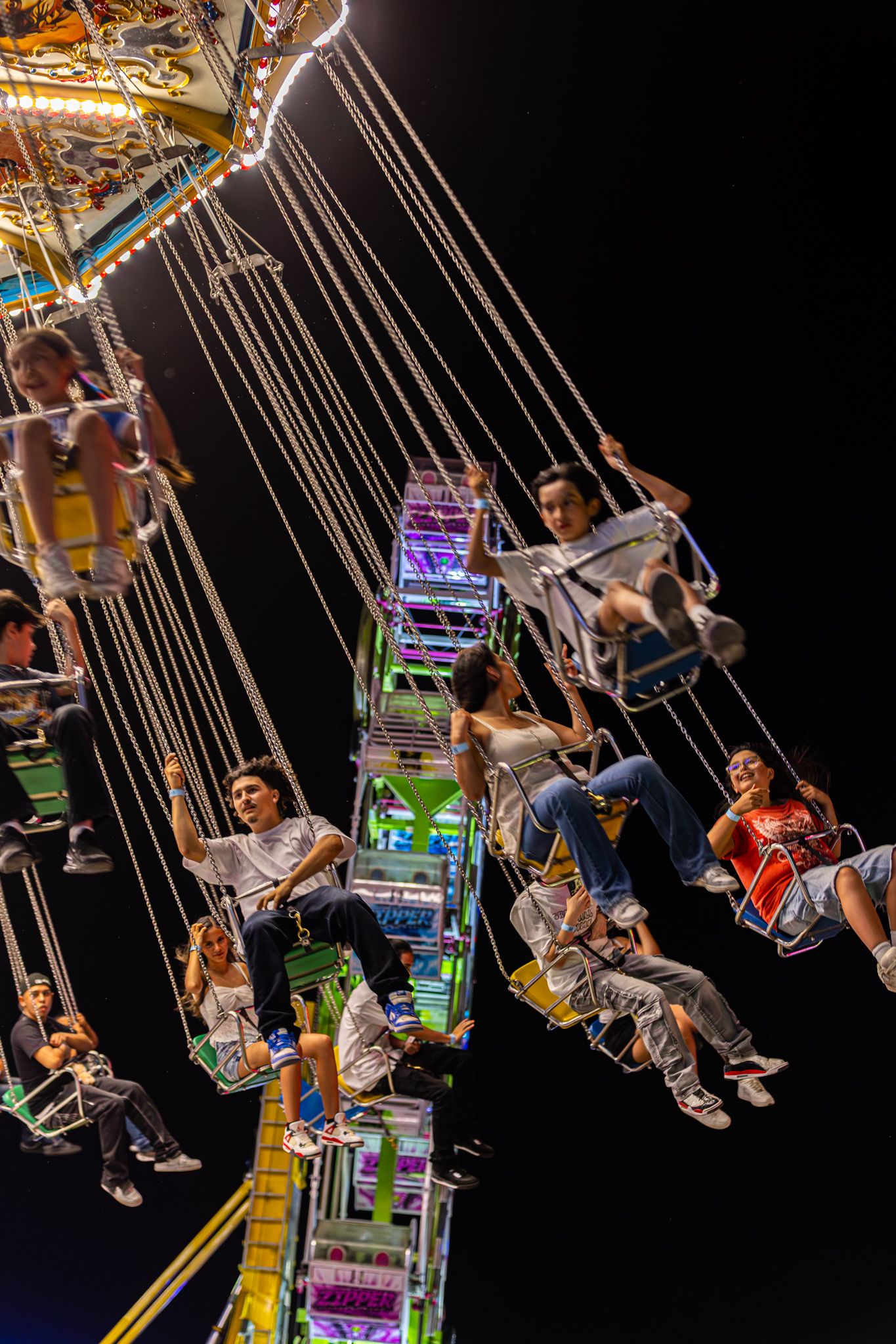 People enjoying a colorful illuminated swing carousel ride at night against a dark sky at an amusement park.