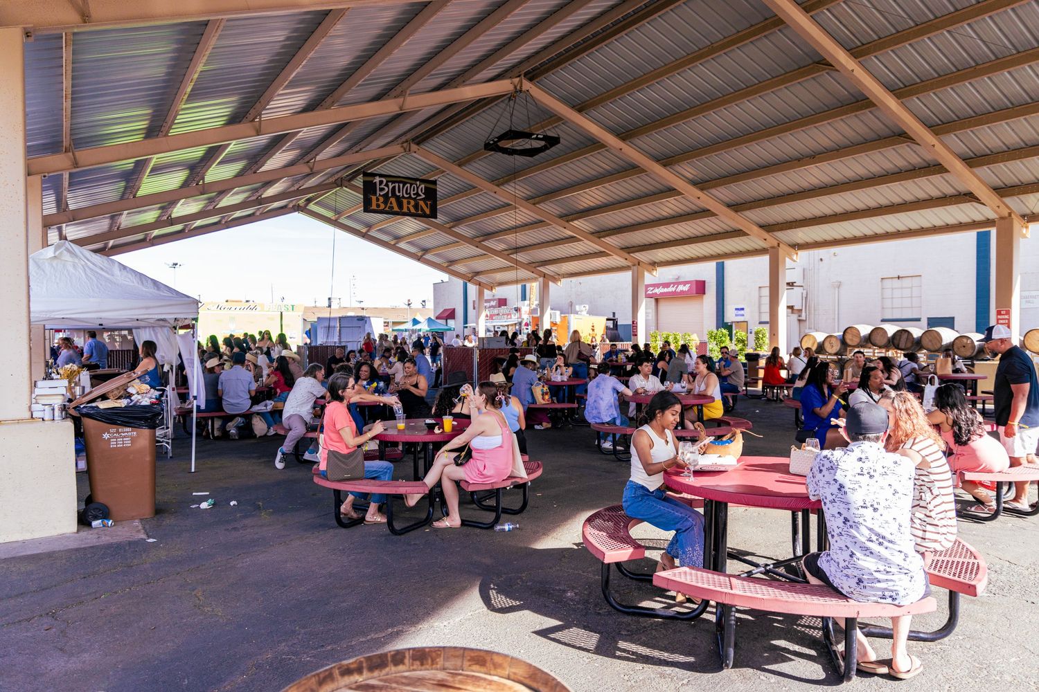 A large outdoor food festival with crowds of people dining at pink picnic tables under a covered pavilion.