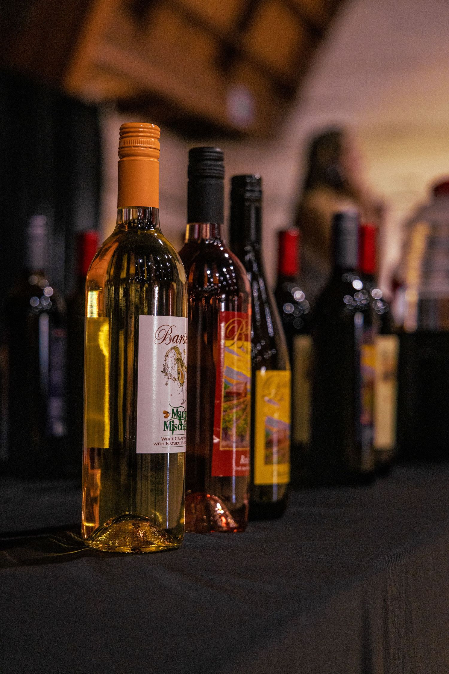 Assorted wine bottles displayed on a dark table at an indoor wine tasting event with warm ambient lighting.
