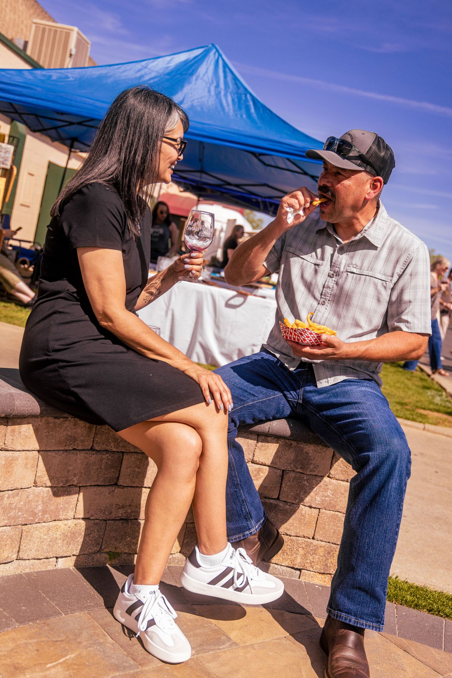 A couple sitting outdoors sharing food and wine at a sunny outdoor food and wine festival.