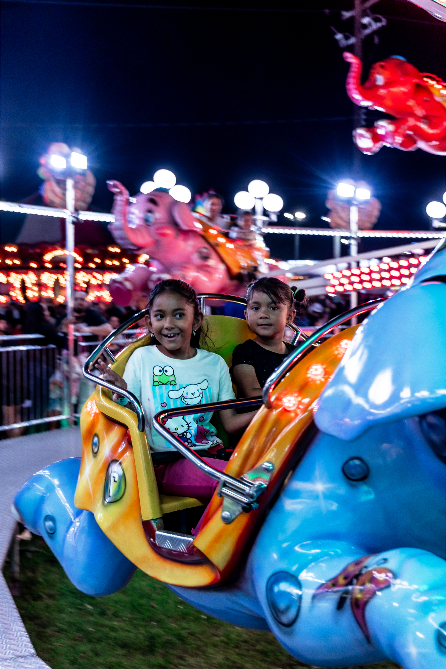 Two happy children riding a colorful carnival ride at a night fair with bright lights.
