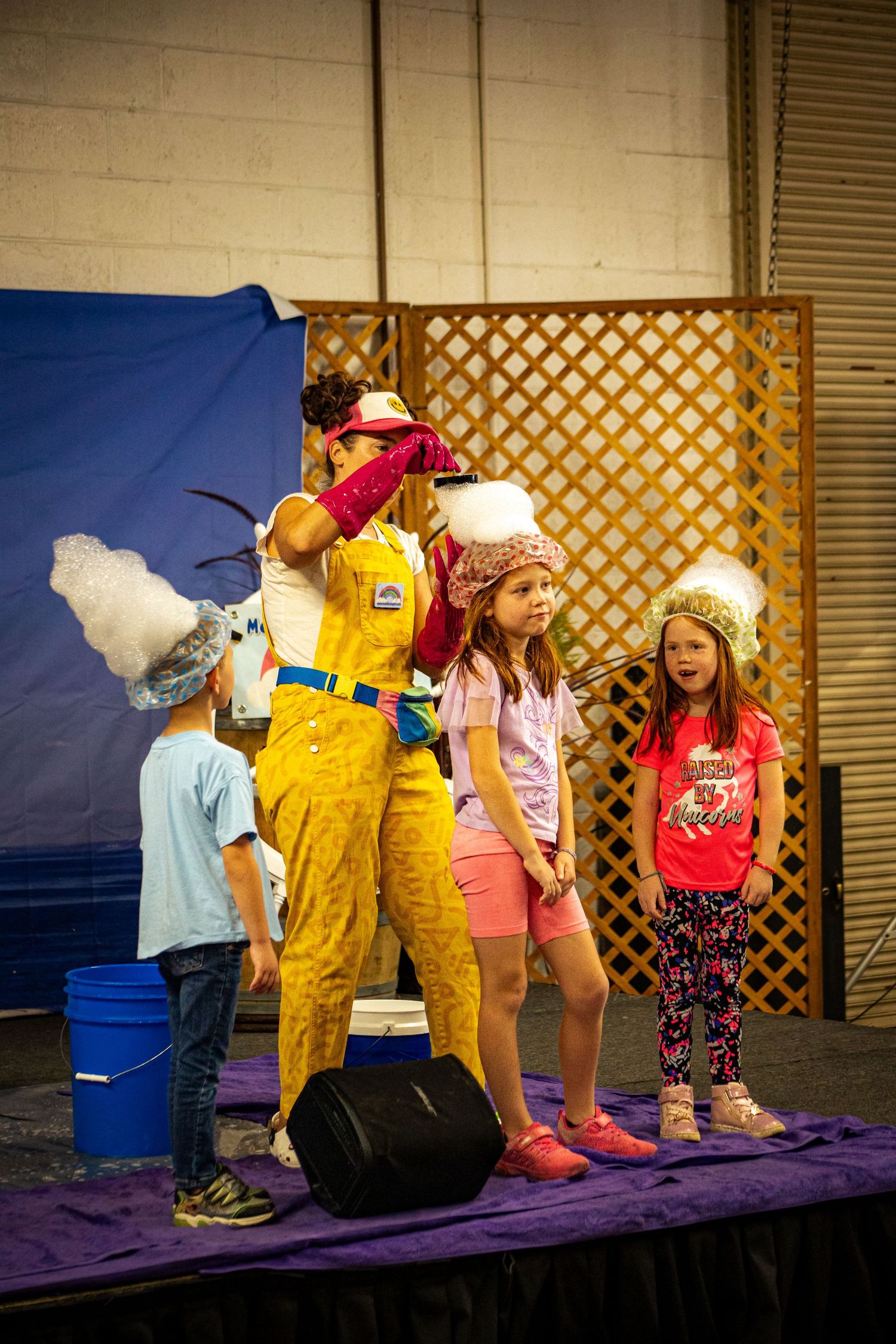 Performer in yellow costume entertains children on stage at a colorful kids show event indoors.