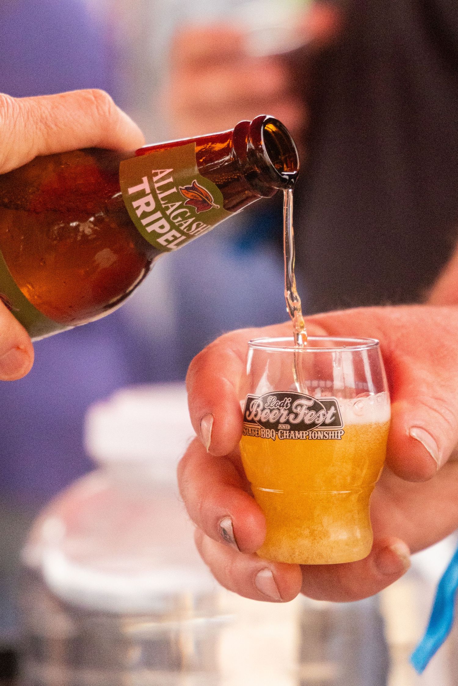 Beer being poured from a Tripel bottle into a Beer Fest championship glass at a festival.