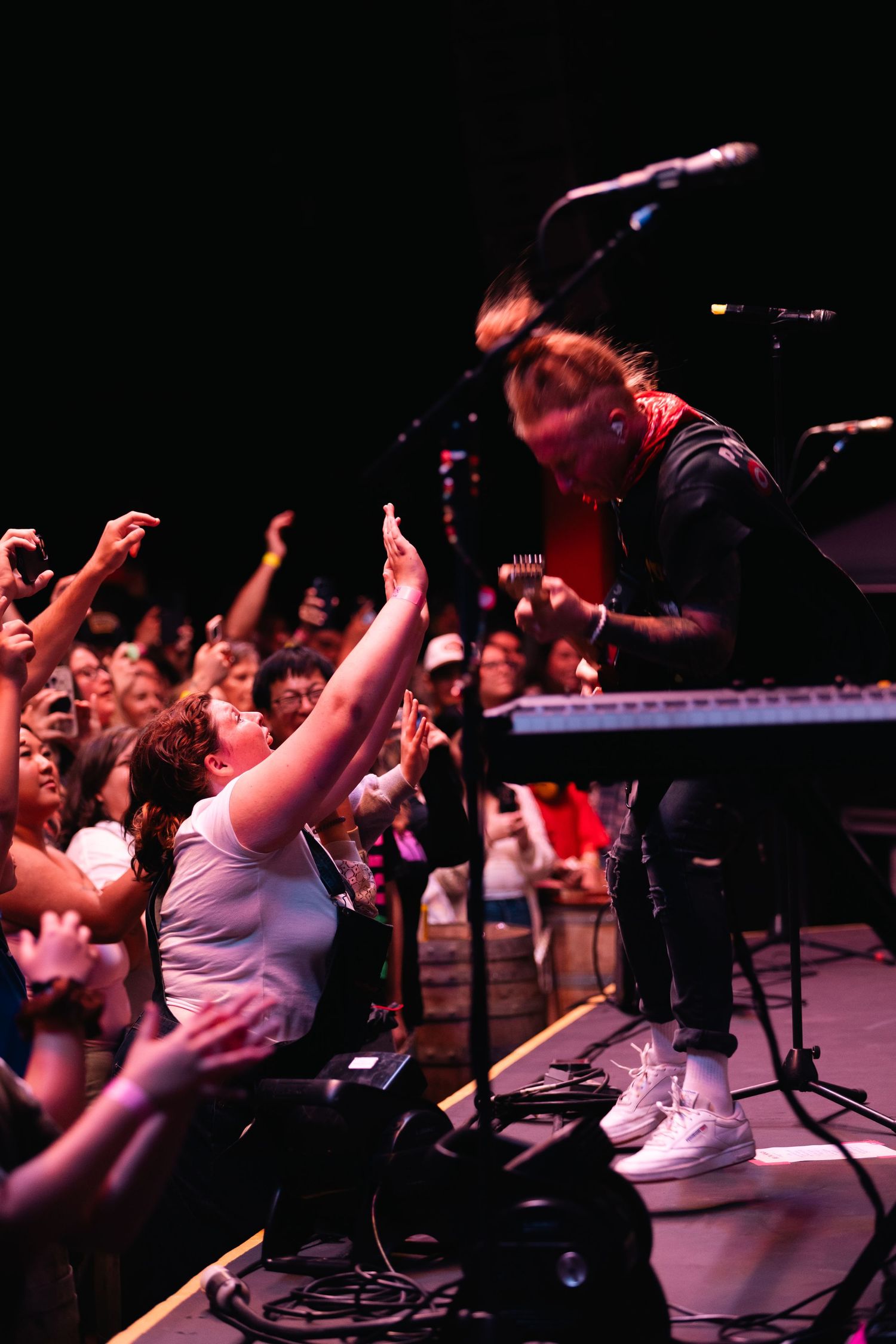 Rock performer leans toward excited fans reaching up from the crowd during an energetic live concert.