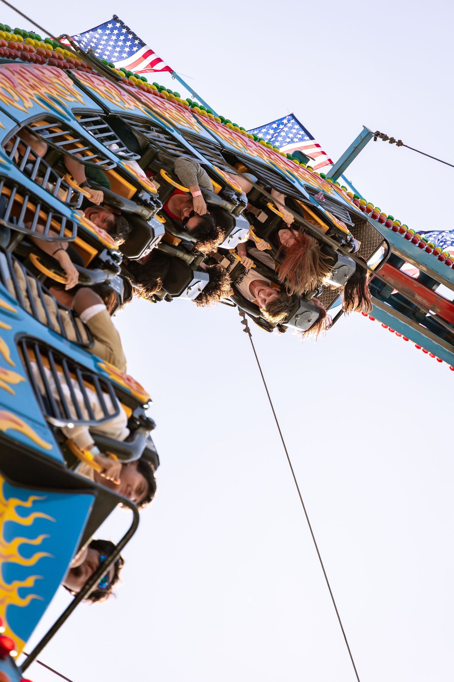 Riders hanging upside down on a thrilling carnival ride with American flags above.
