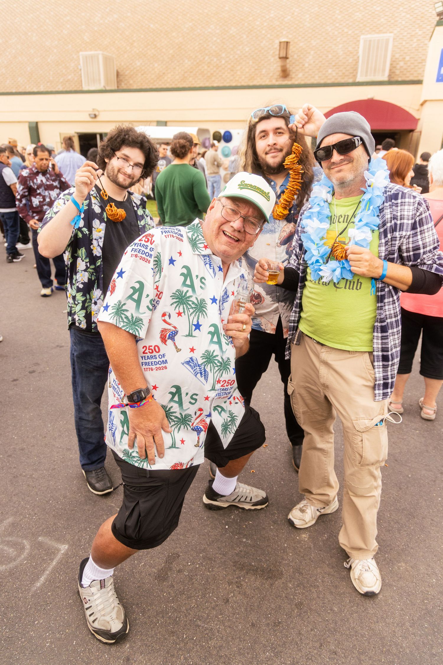 Four men in festive attire, including Hawaiian shirts and leis, pose together at an outdoor event.