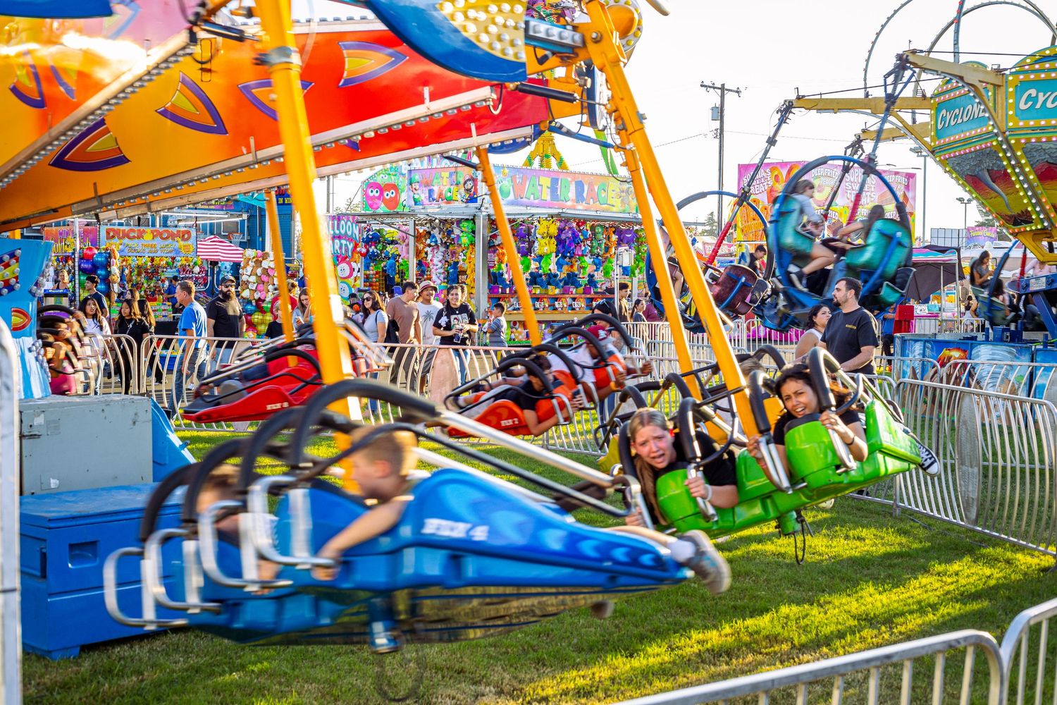Colorful carnival swing ride with excited riders at a lively outdoor fair on a sunny day.