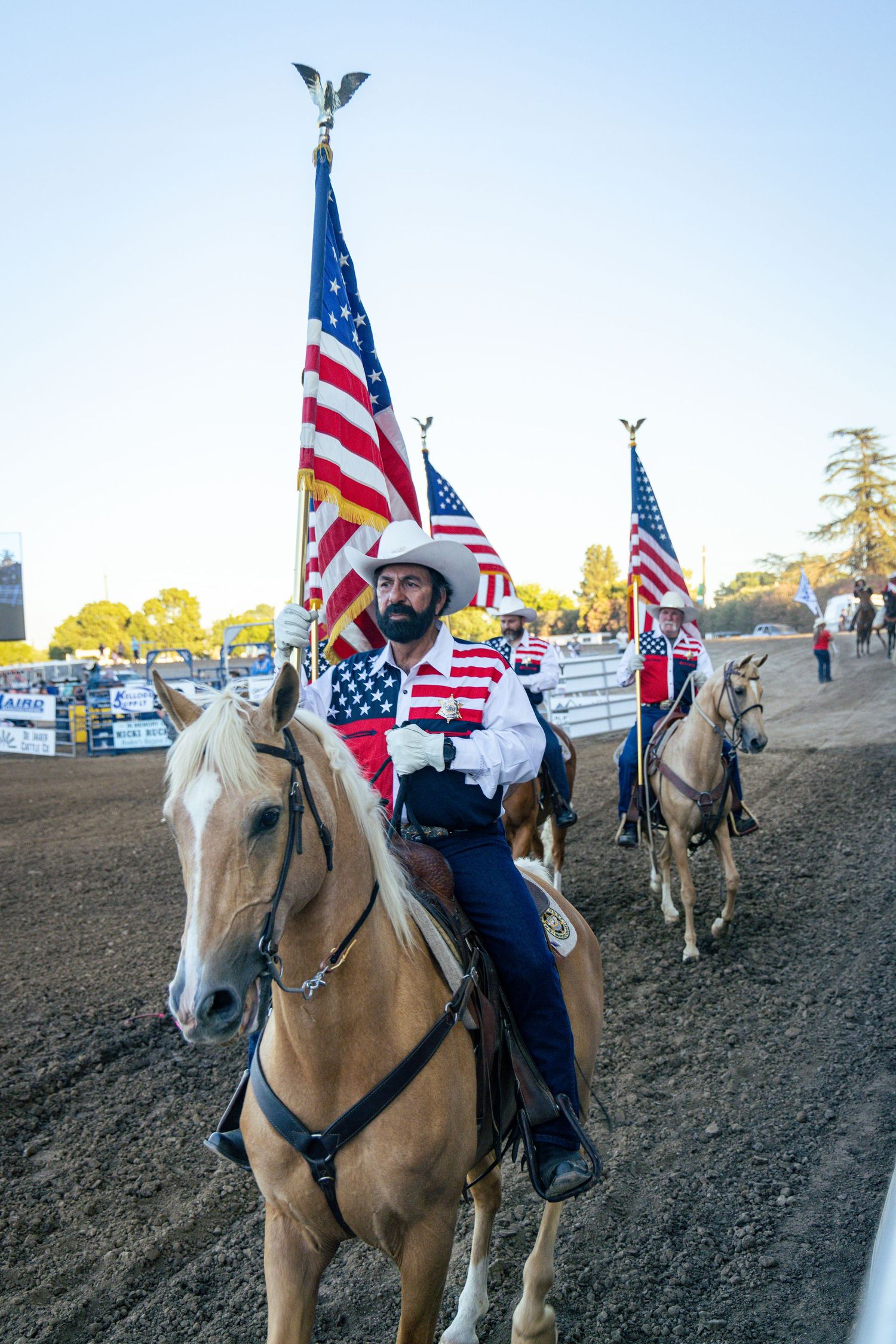 Cowboys on horseback carrying American flags at a rodeo opening ceremony.