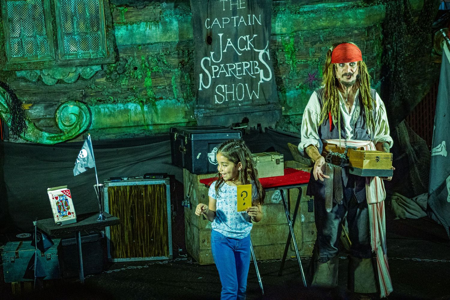 A child participates in Captain Jack Sparrow's live show on stage at a Pirates of the Caribbean themed attraction.