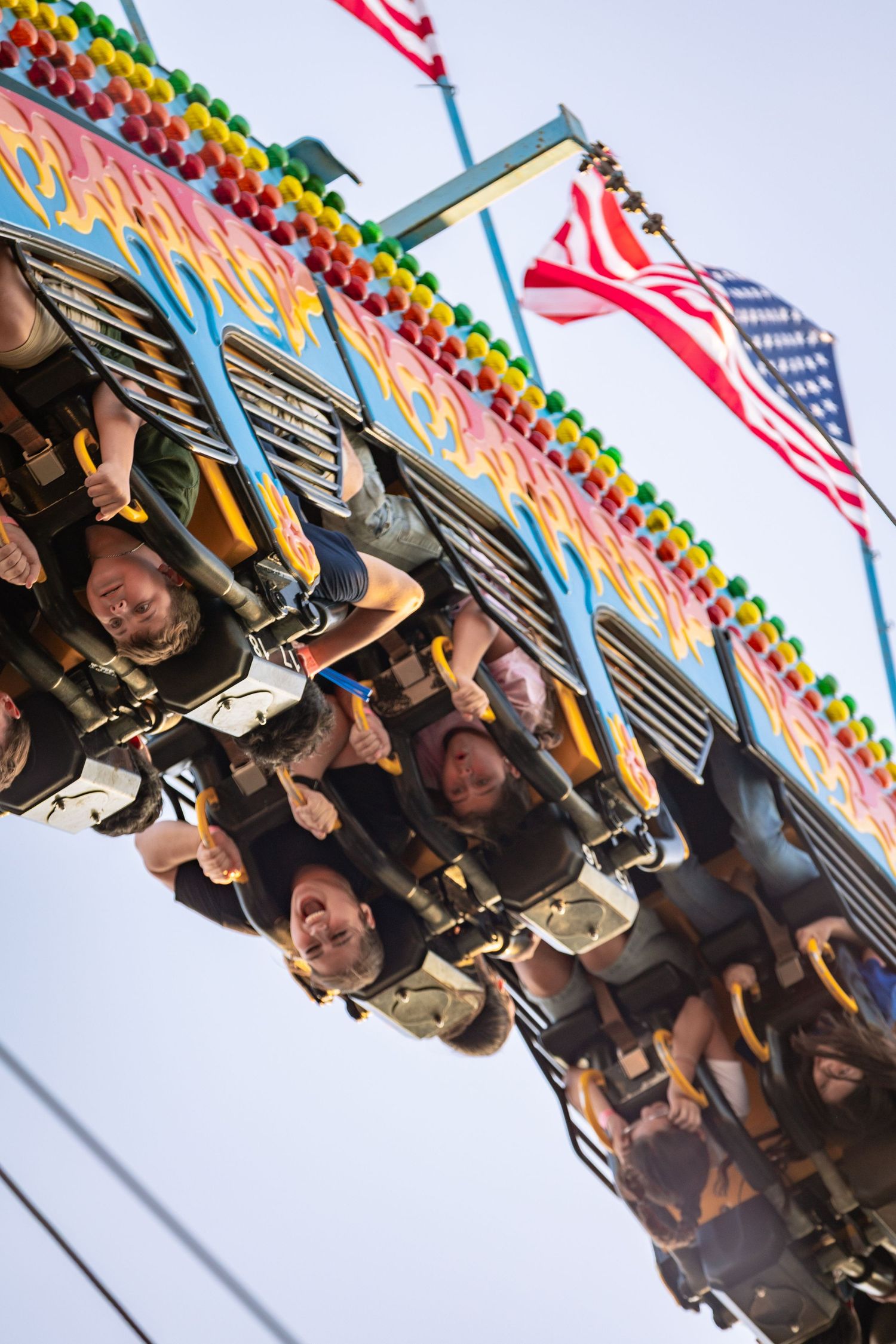 Smiling riders flipped upside down on a colorful carnival thrill ride at a fair.