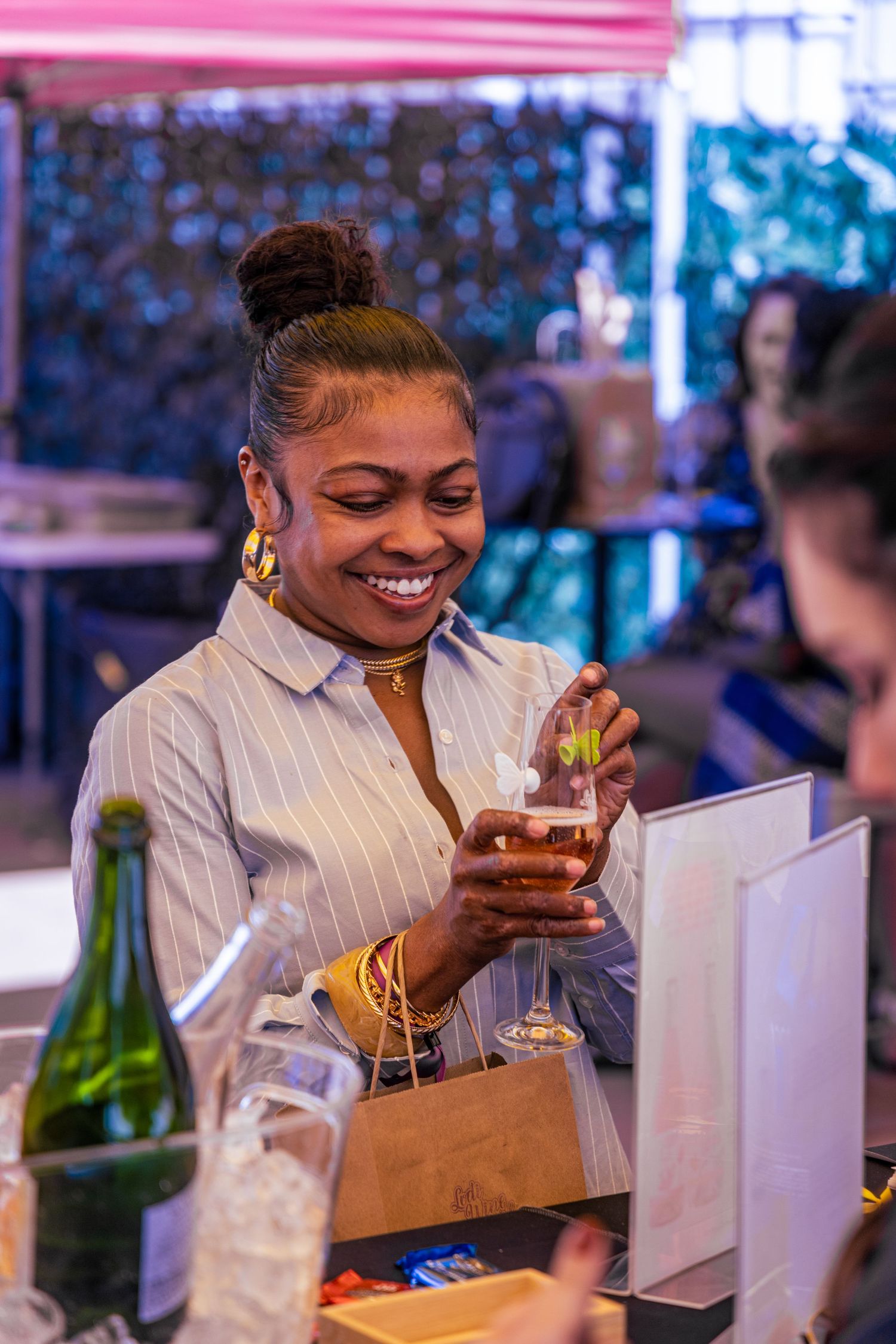 Smiling woman in striped shirt holding a drink at an outdoor food and beverage festival booth.