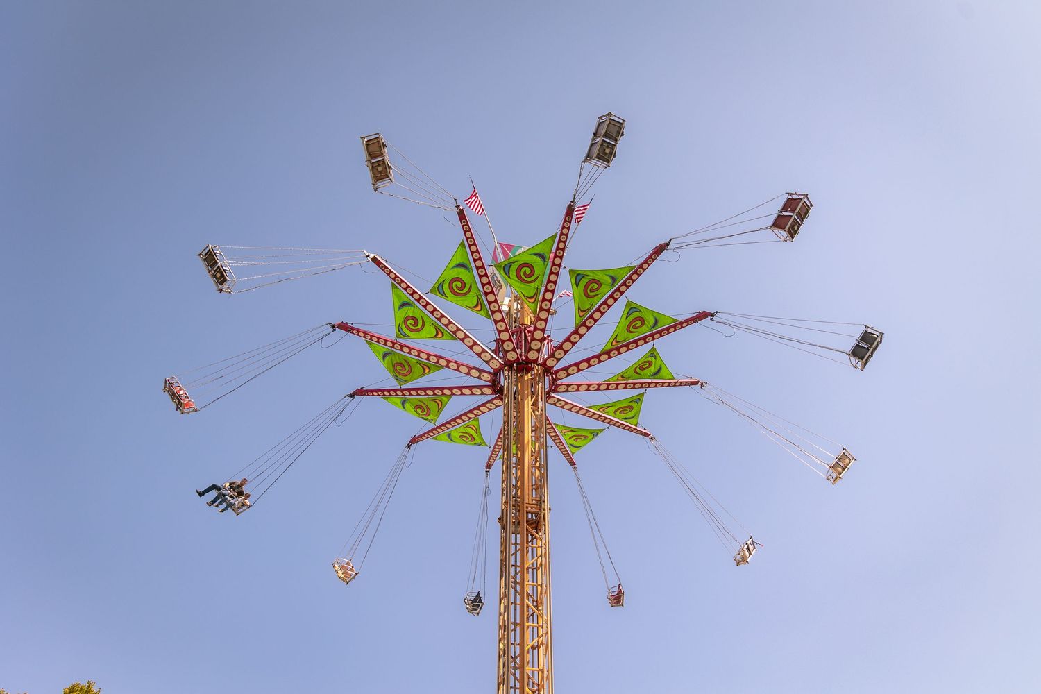 Aerial view of a chain swing carousel ride against a clear blue sky at a fair.
