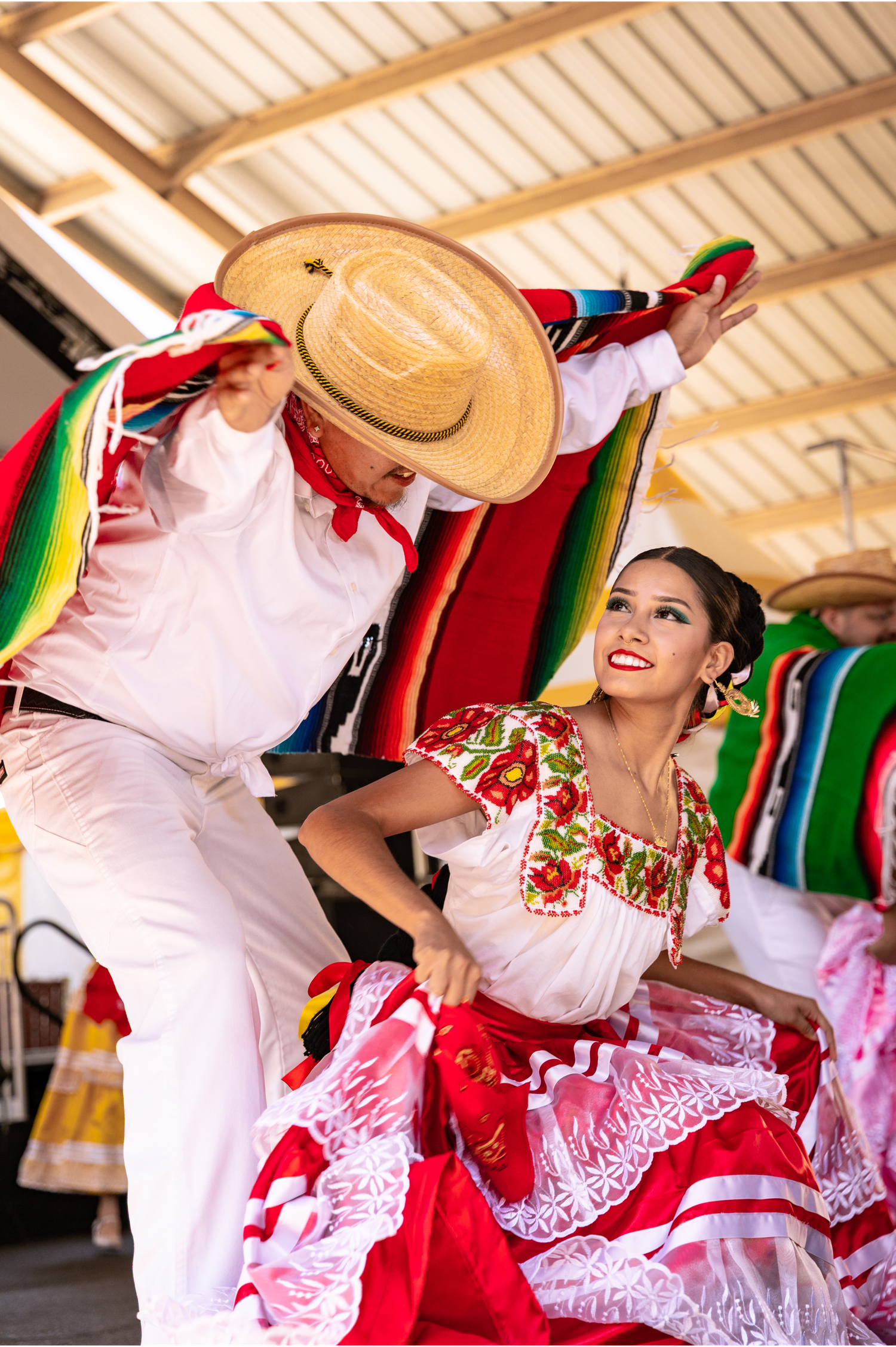 Traditional Mexican folkloric dancers performing Jarabe Tapatio in colorful costumes on stage.