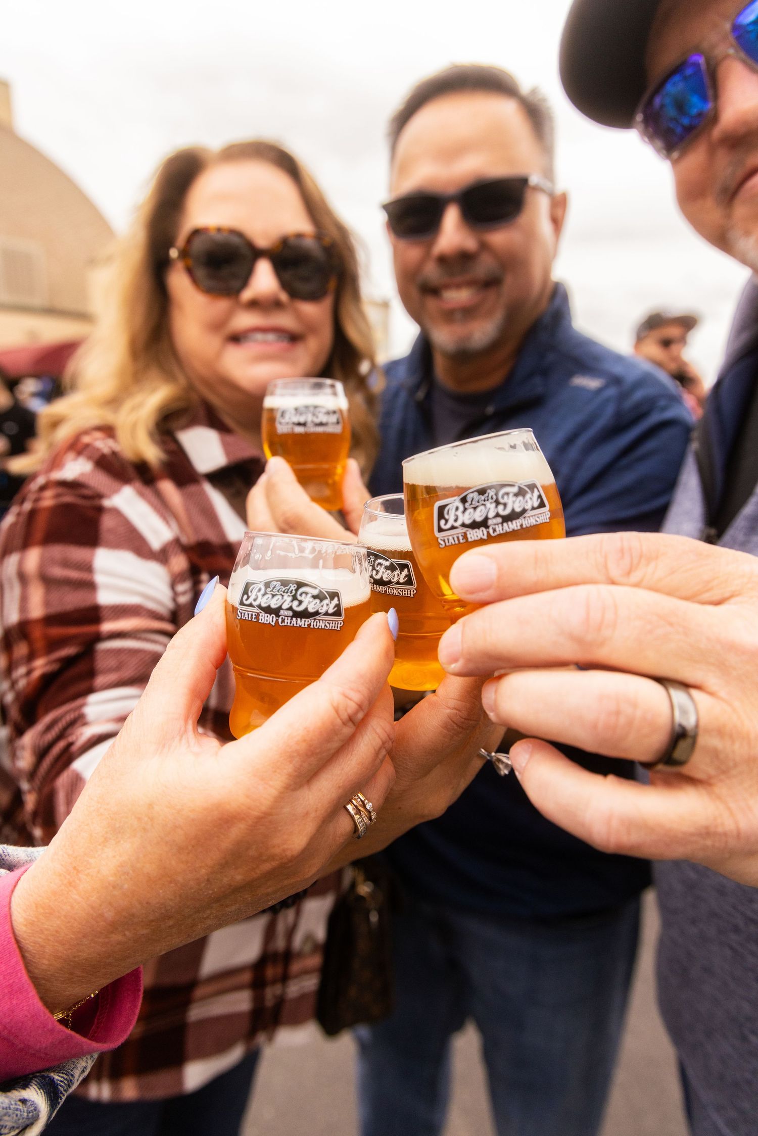 Friends toasting with BeerFest tasting glasses at an outdoor craft beer festival event.