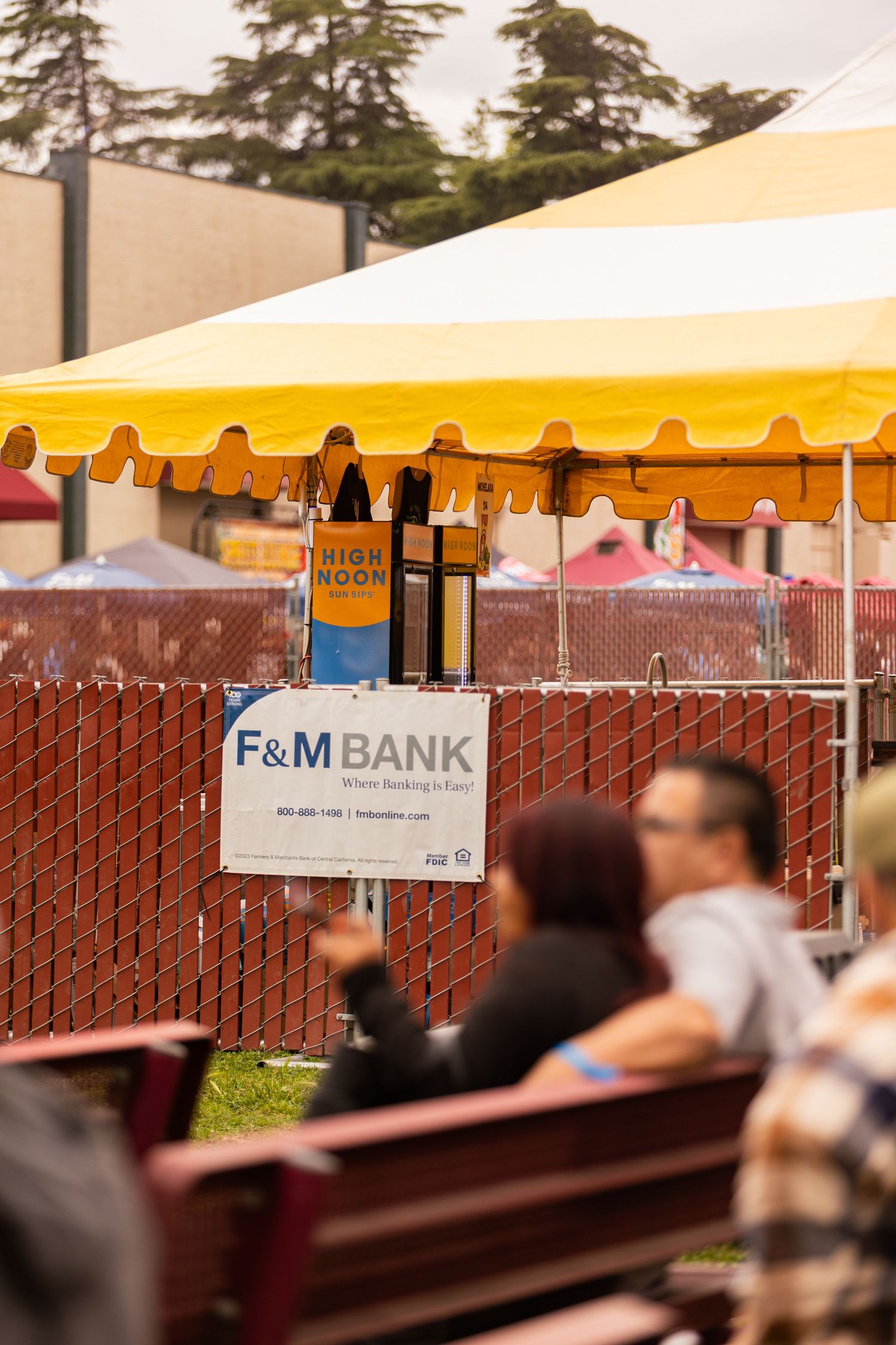 F&M Bank sponsor sign displayed at an outdoor festival beneath a yellow and white striped tent.