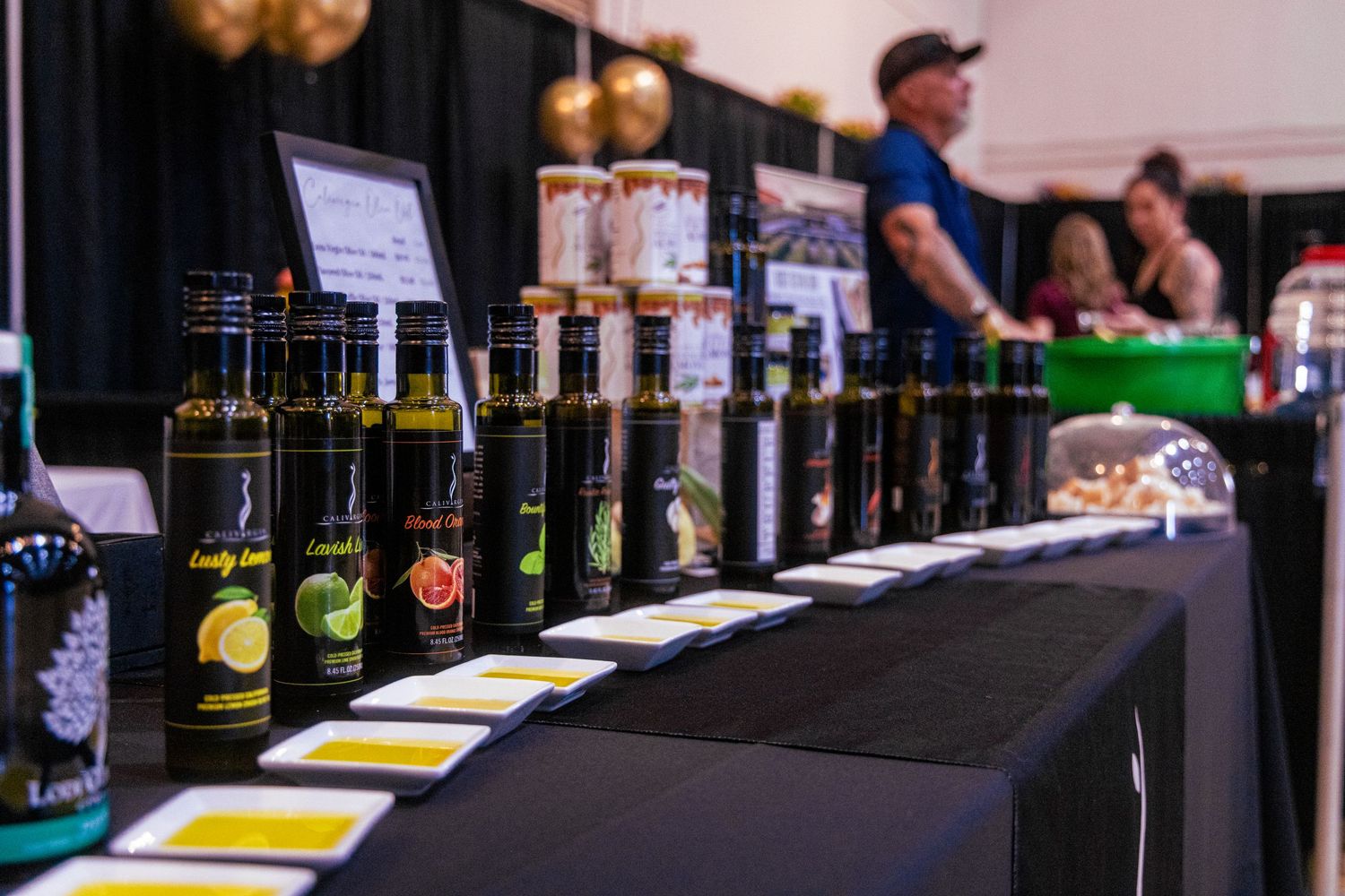 A display of gourmet olive oil bottles with colorful labels lined up on a table at a food festival.