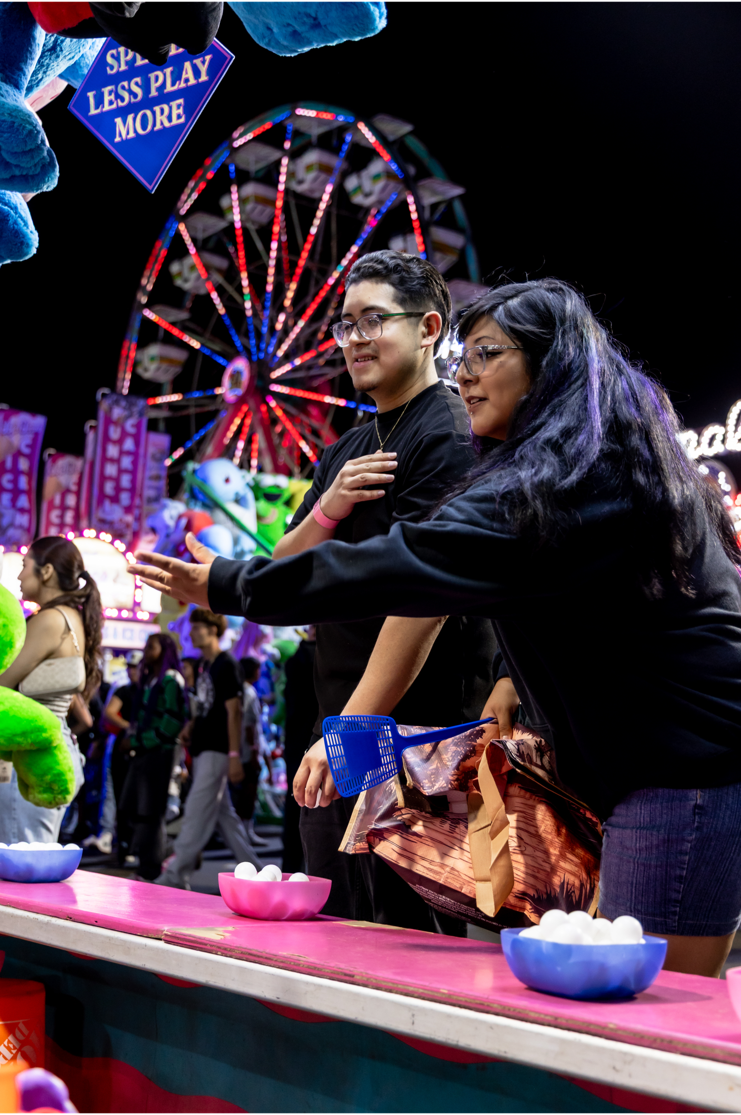 Two young women playing a carnival game at night with a ferris wheel lit up in the background.