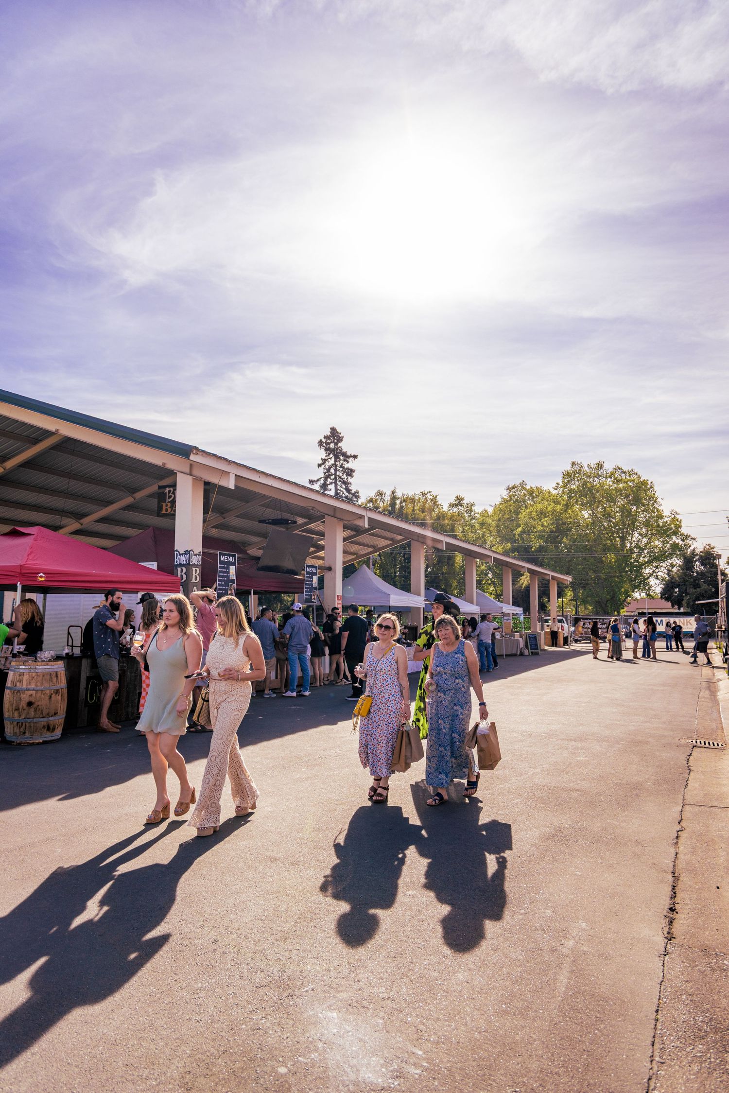 A group of women walking through a sunny outdoor food and wine festival with vendor tents.