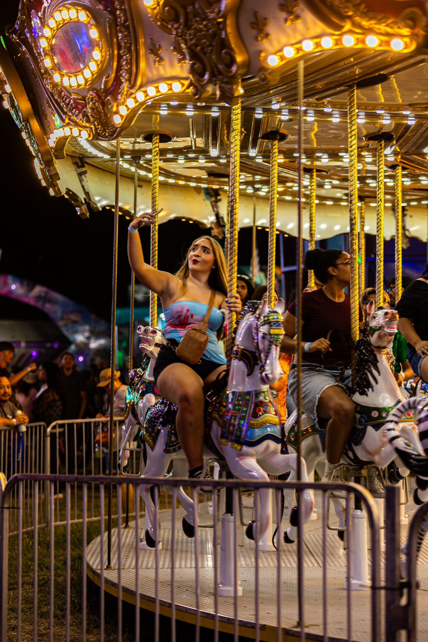 Young woman rides a glowing carousel horse at a county fair at night.
