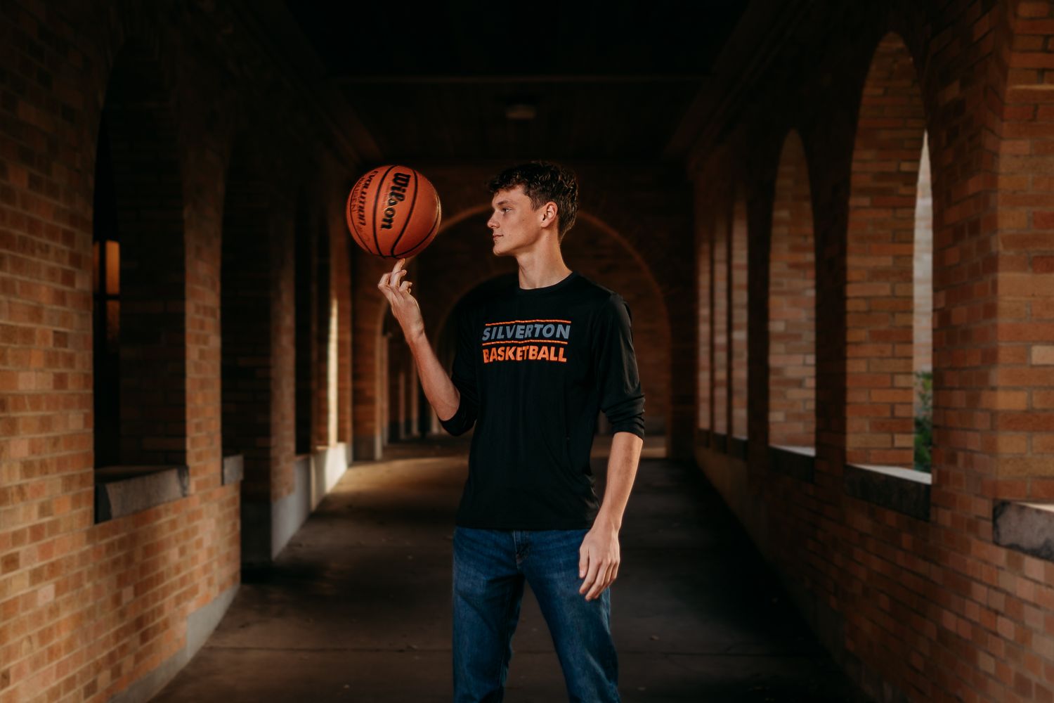 Senior boy spinning basketball on his finger in a walkway.