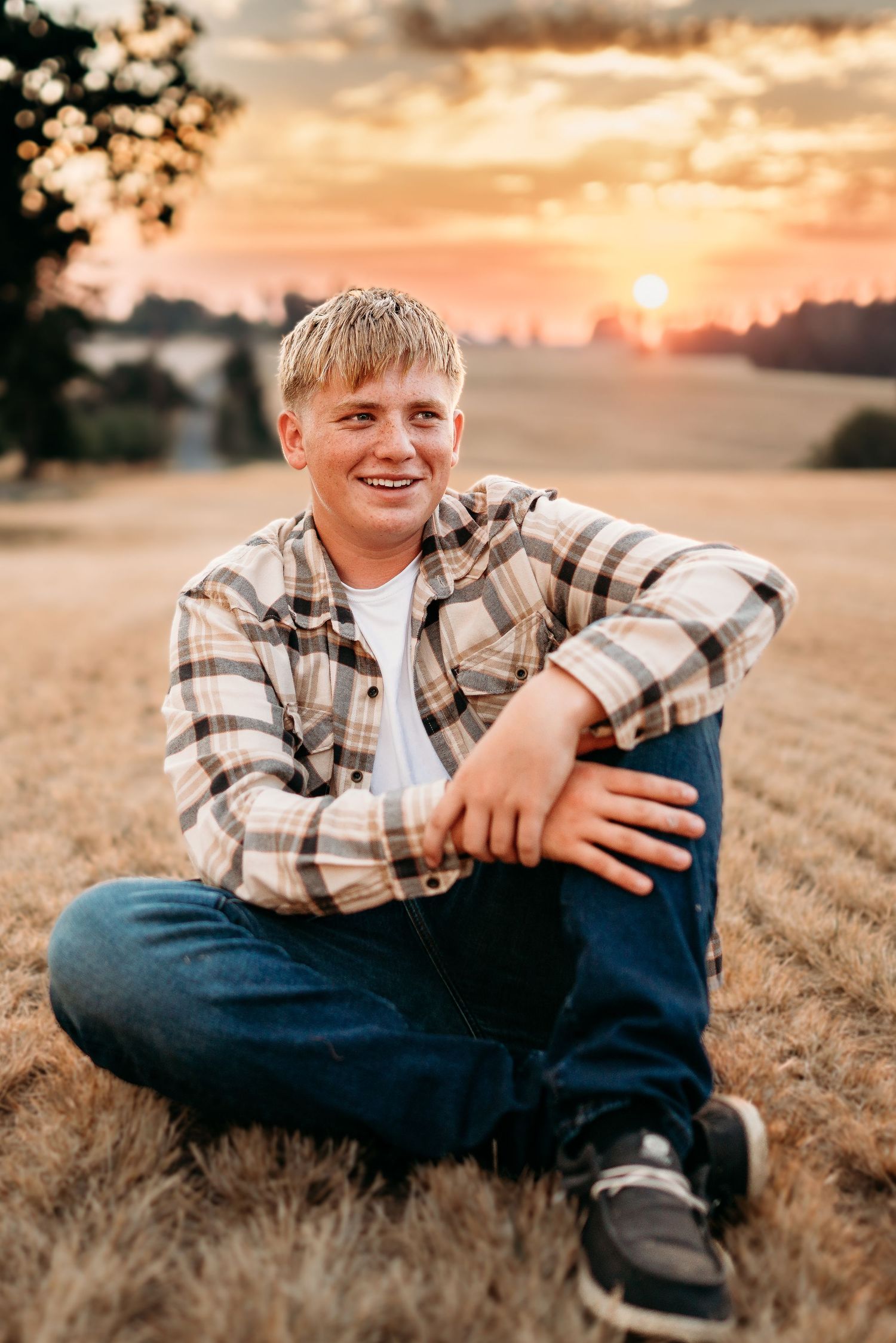 Senior boy sitting in a field at sunset with relaxed smile