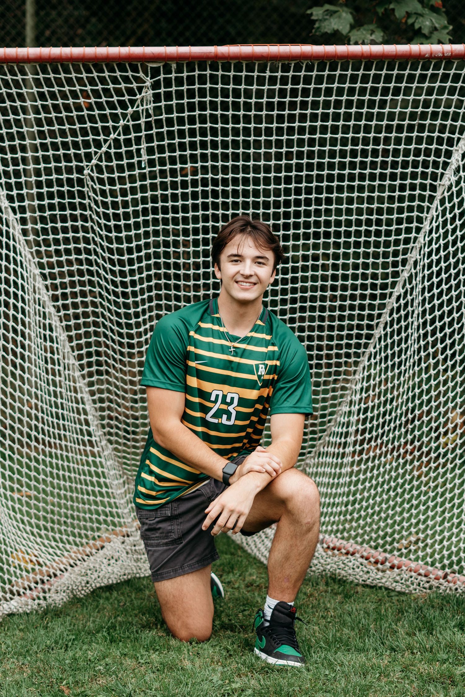Senior boy kneeling in front of a soccer goal wearing his uniform