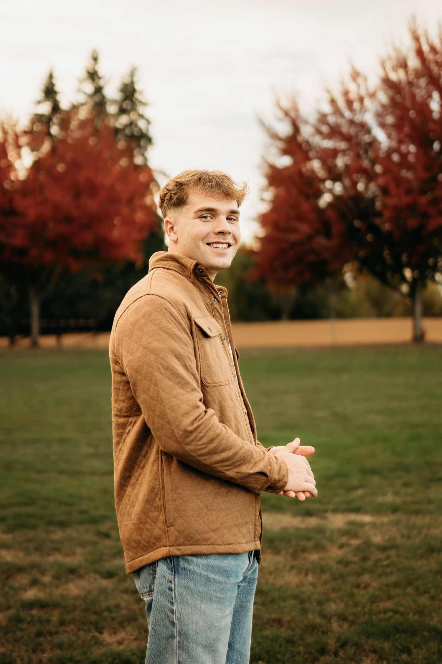 Senior boy smiling with autumn trees in the background