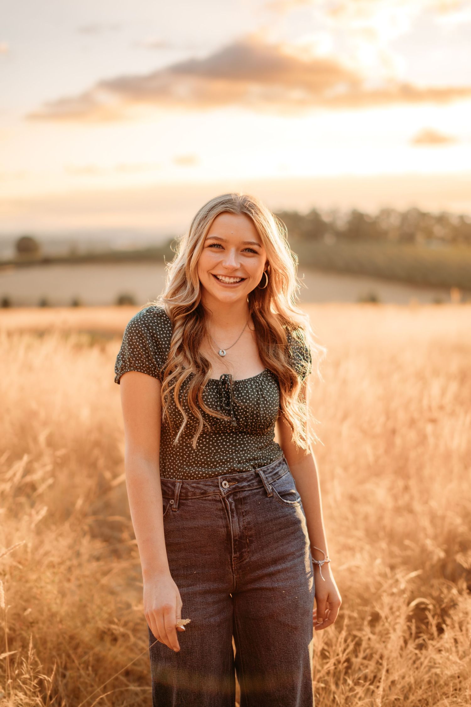 Senior girl standing in tall grass at sunset, smiling