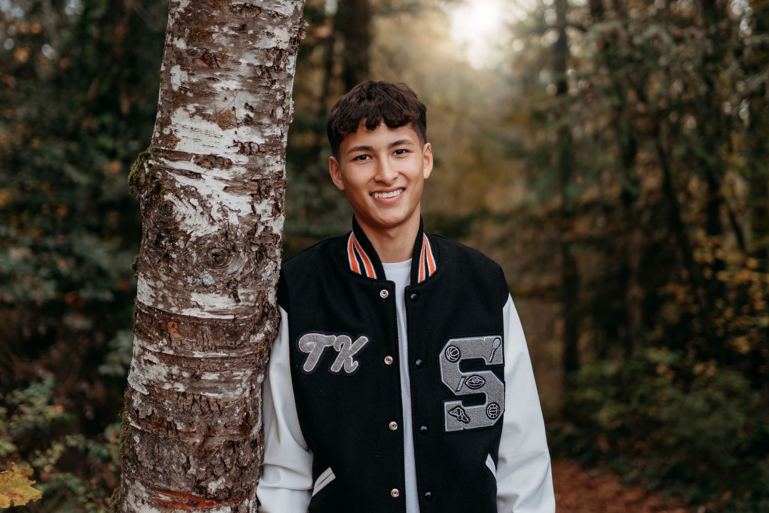 Senior boy standing outdoors beside a tree, smiling