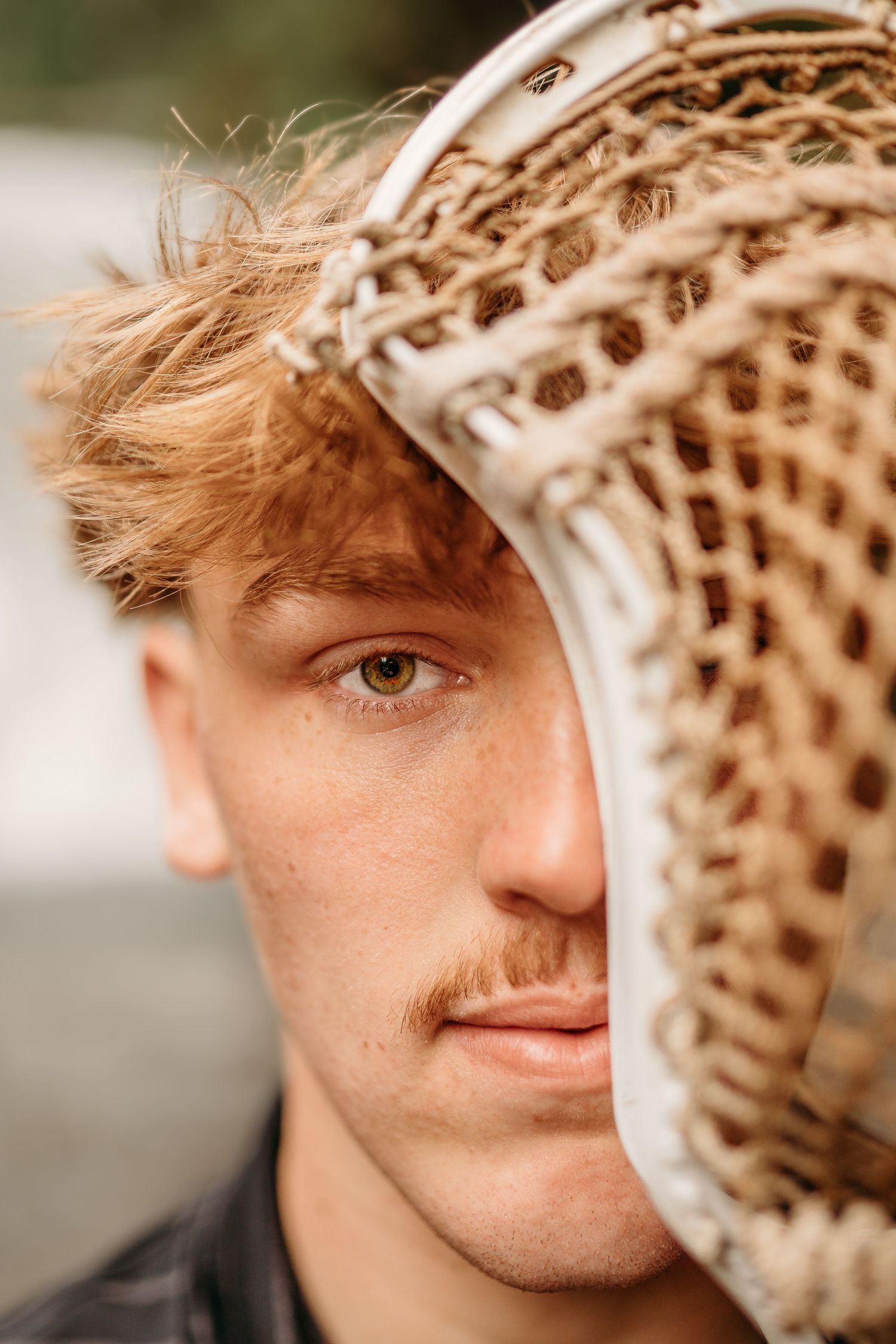 Senior boy holding his lacrosse stick in front of his face