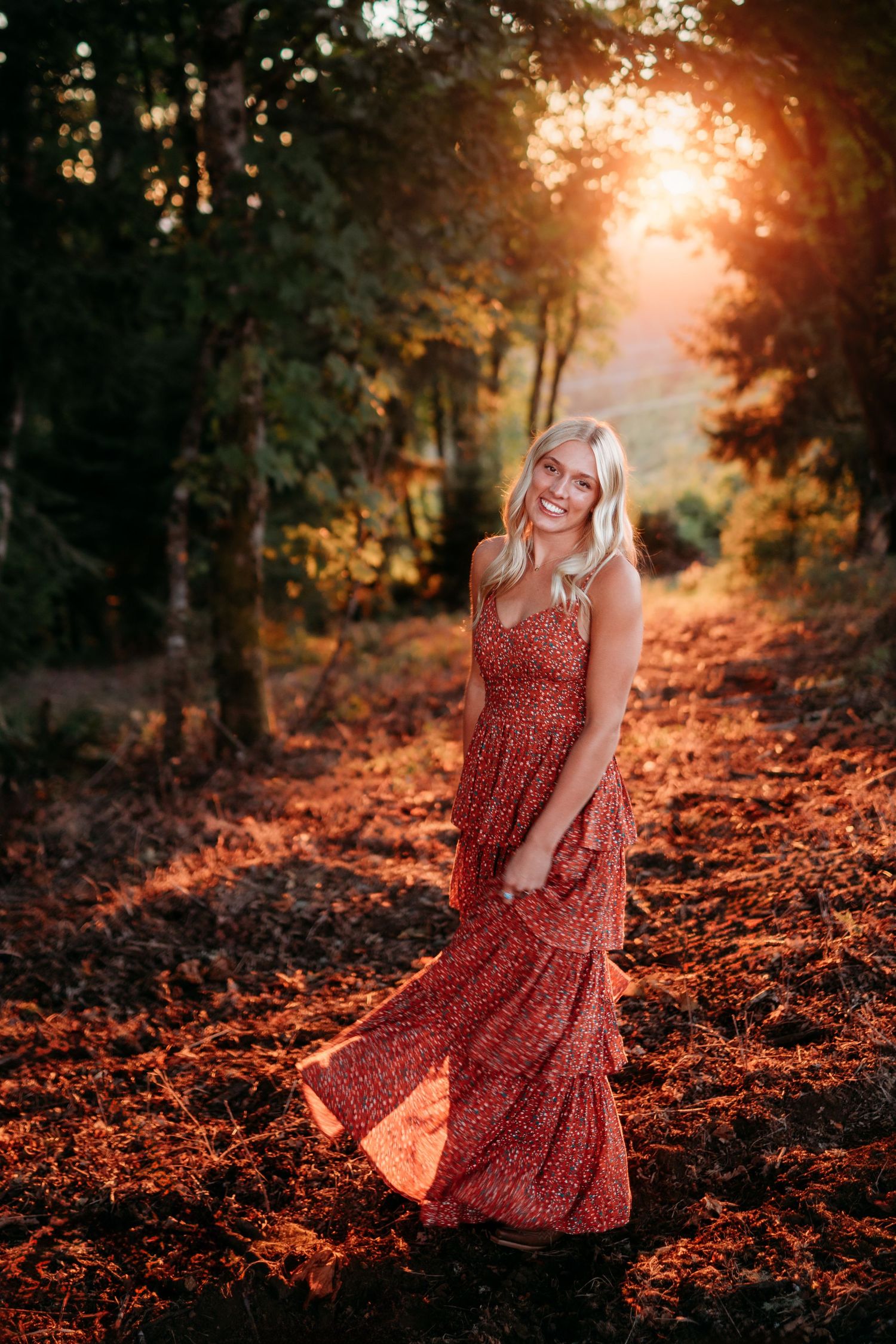 High school senior portrait of girl walking through fall leaves in a flowing dress at sunset