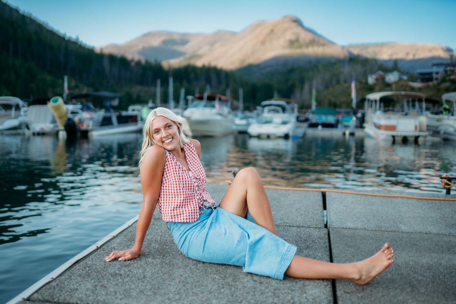 Senior girl sitting on a dock at Detroit Lake Oregon with mountains in the background