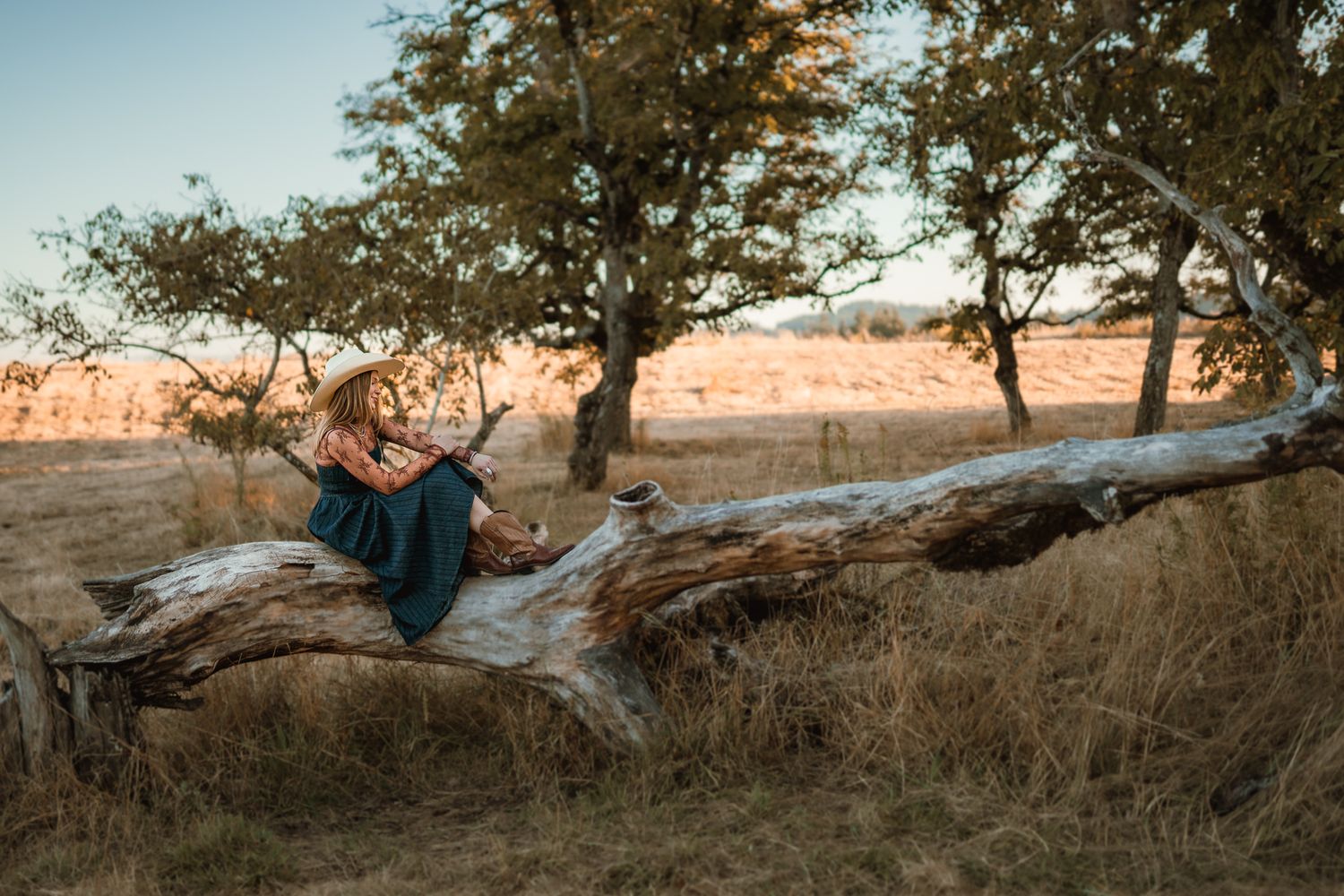 Girl sitting on tree limb with cowboy hat and cowboy boots