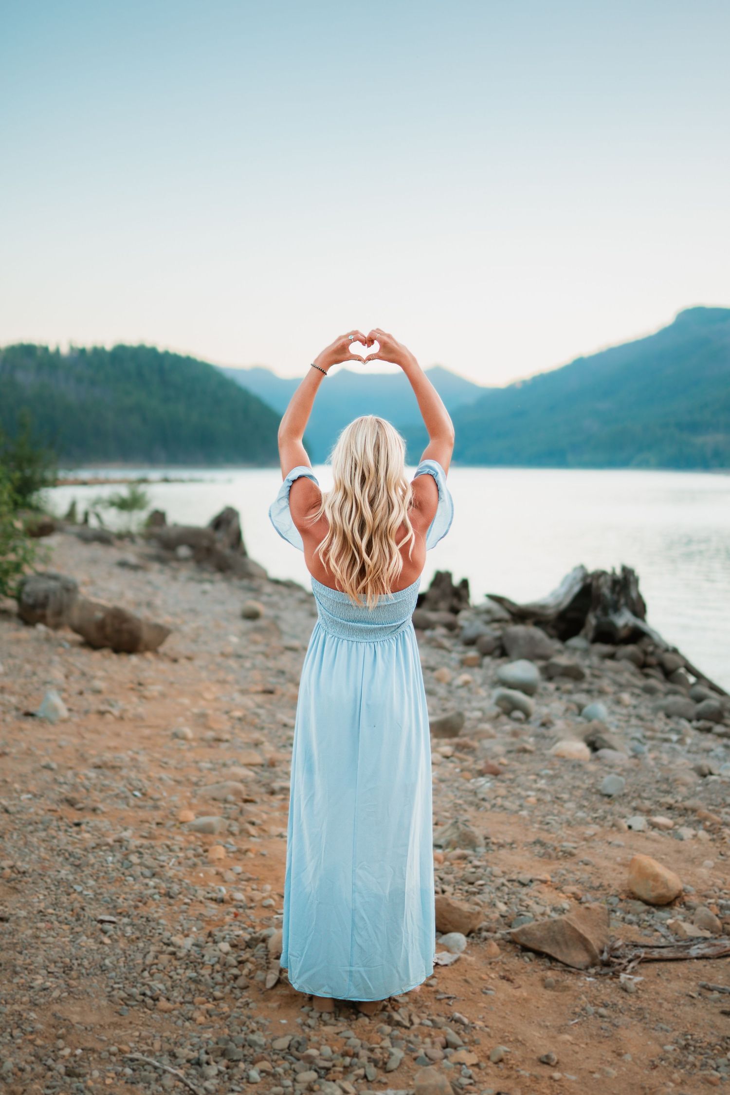 A senior girl standing with the river in the background, making a heart with her hands.