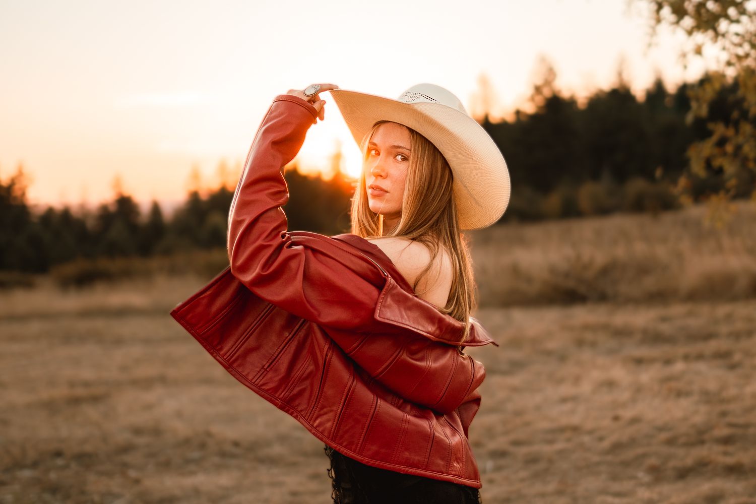 Senior girl holding her cowboy hat with the sunset behind her